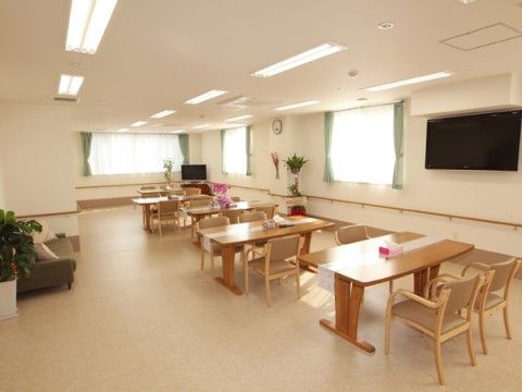 壁に大型のテレビが設置され、揃いのテーブルセットが三台並んでいるリビング