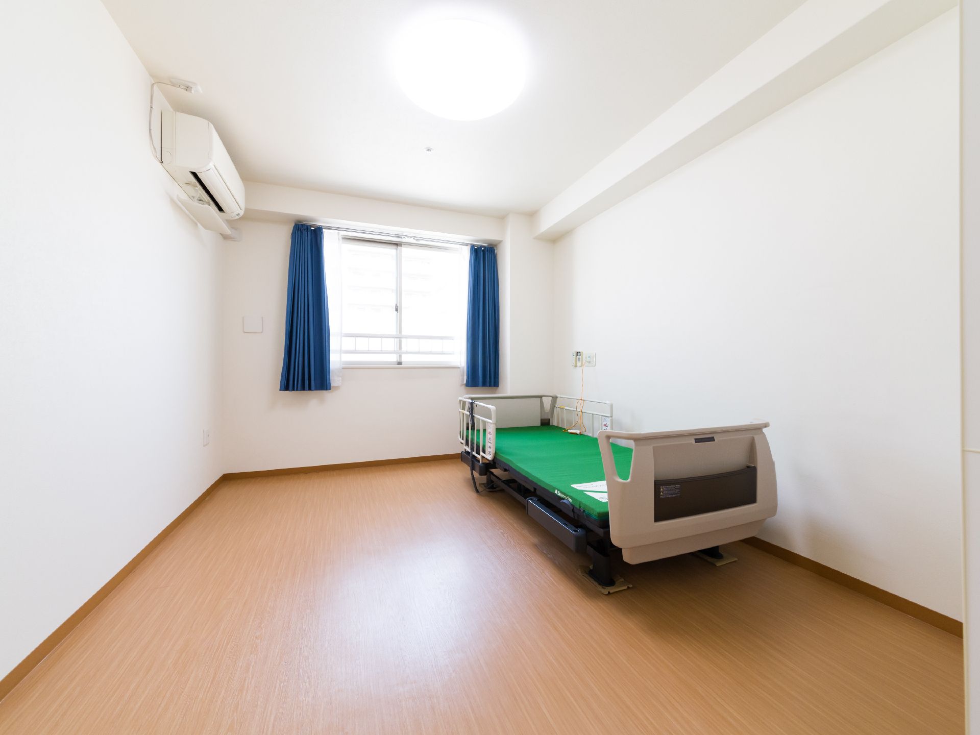 ワンルームながらも広い部屋になっている。施設から貸し出しされる転落防止の介護ベッドが設けられている。