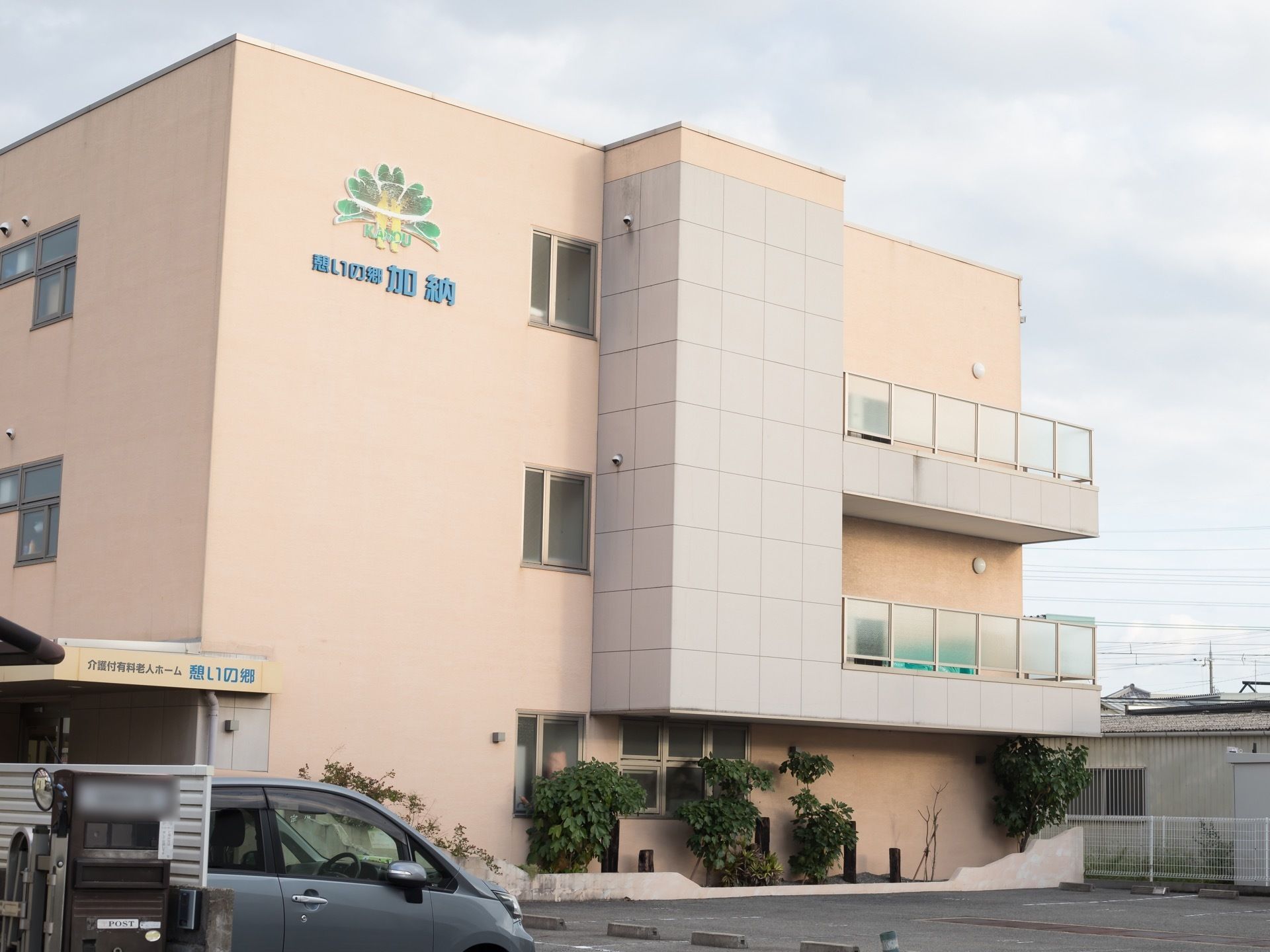 淡いベージュ調の3階建ての施設外観になっている。施設内には駐車スペースが用意されており、車が1台停まっている。