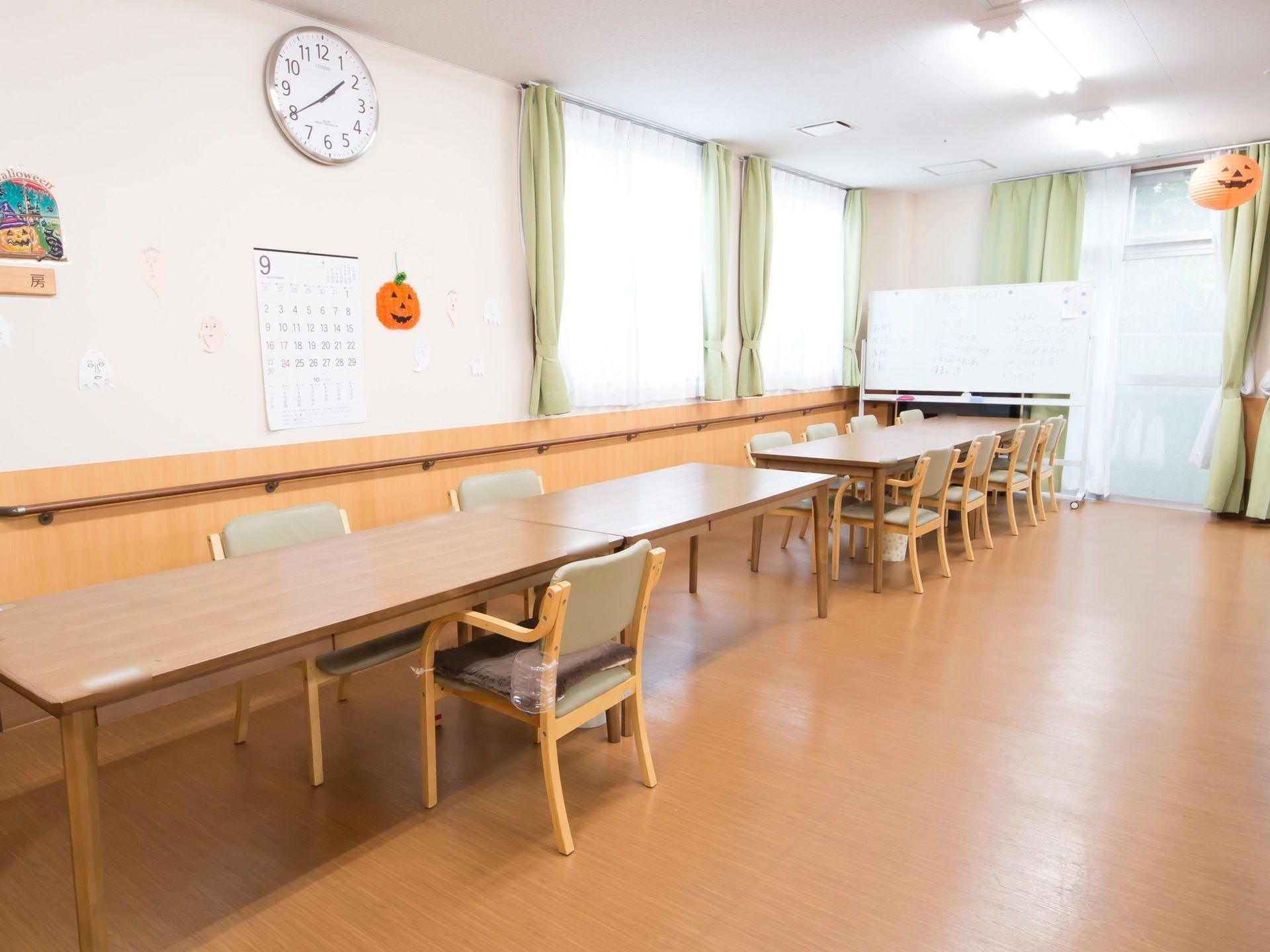 食堂の壁には丸い時計がかけられている。長机が２つくっつけられたものが２セット置かれており、周りには椅子が並べられている。