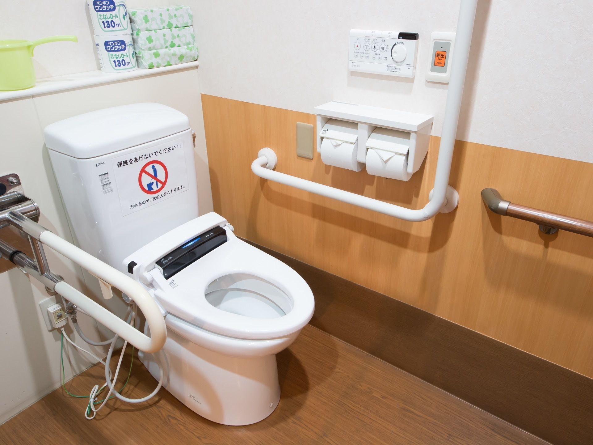 トイレには洋式便器が設置されており、タンクに使用時の注意書きの紙が貼られている。壁側には手すりが設けられている。
