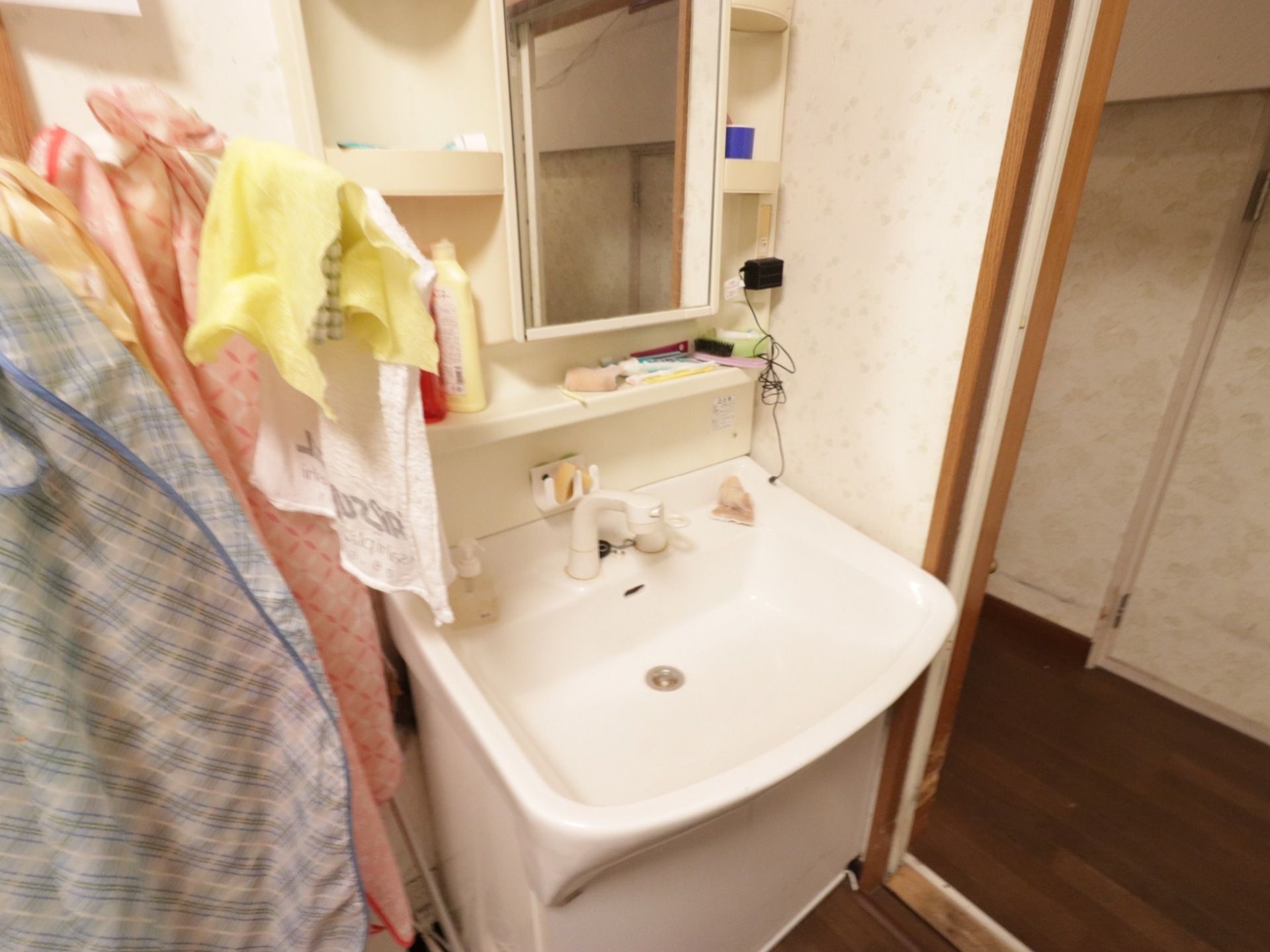 共用の洗面台には鏡の周りに小物置場などが用意されている。洗面台の横には洗濯物を干す台が置かれている。