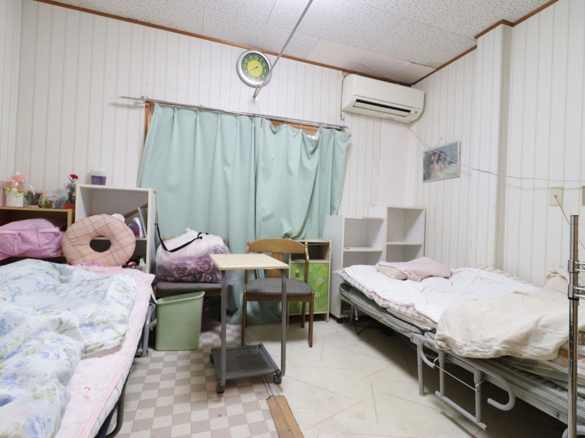 ２人部屋の一例。壁際にベッドが置かれており、窓際にカラーボックスが並べられている。エアコンが完備されている。