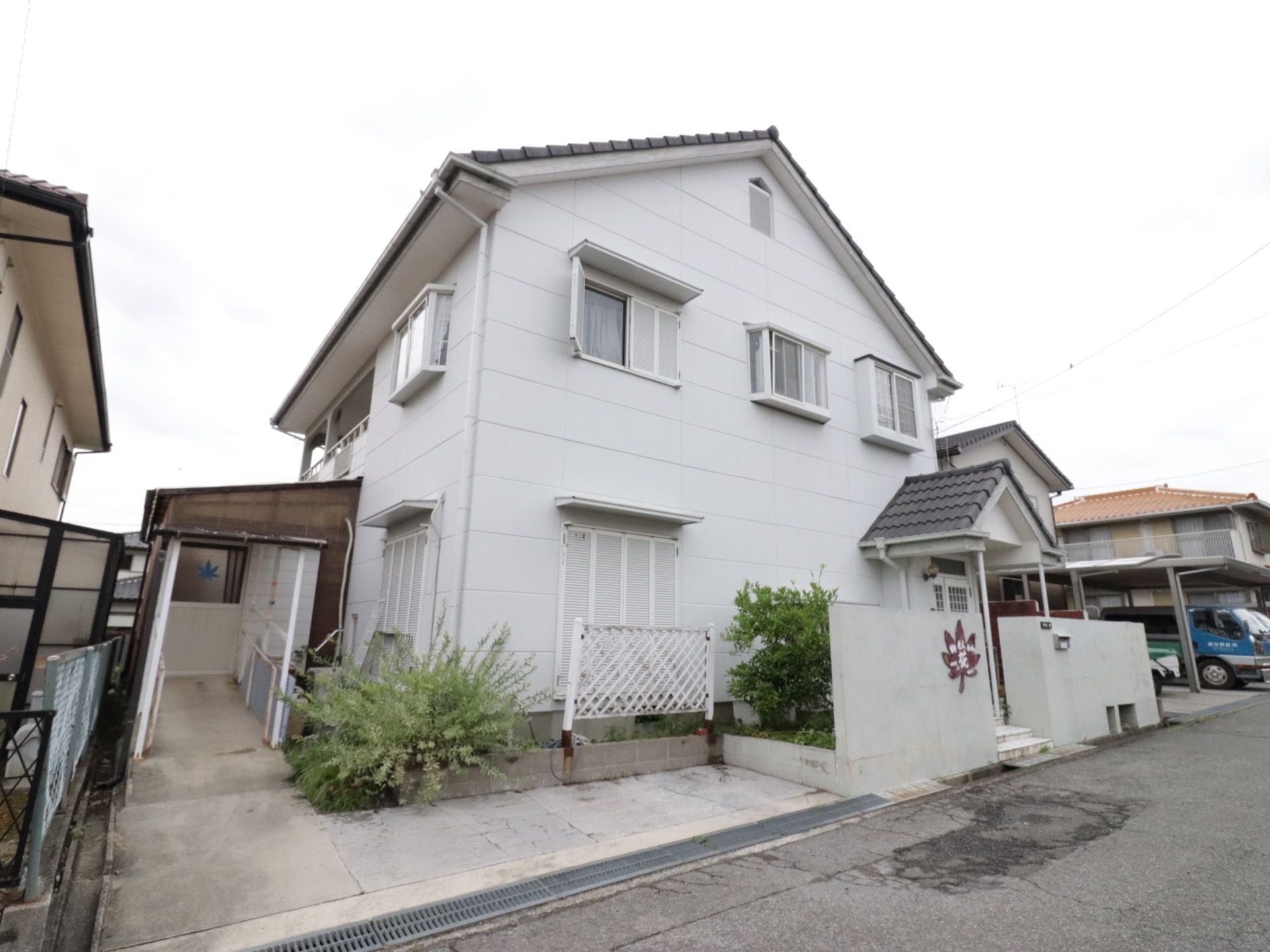 白い三角屋根の２階建ての施設である。塀に施設名をかたどったもみじのロゴが表示されている。玄関までスロープが続いている。
