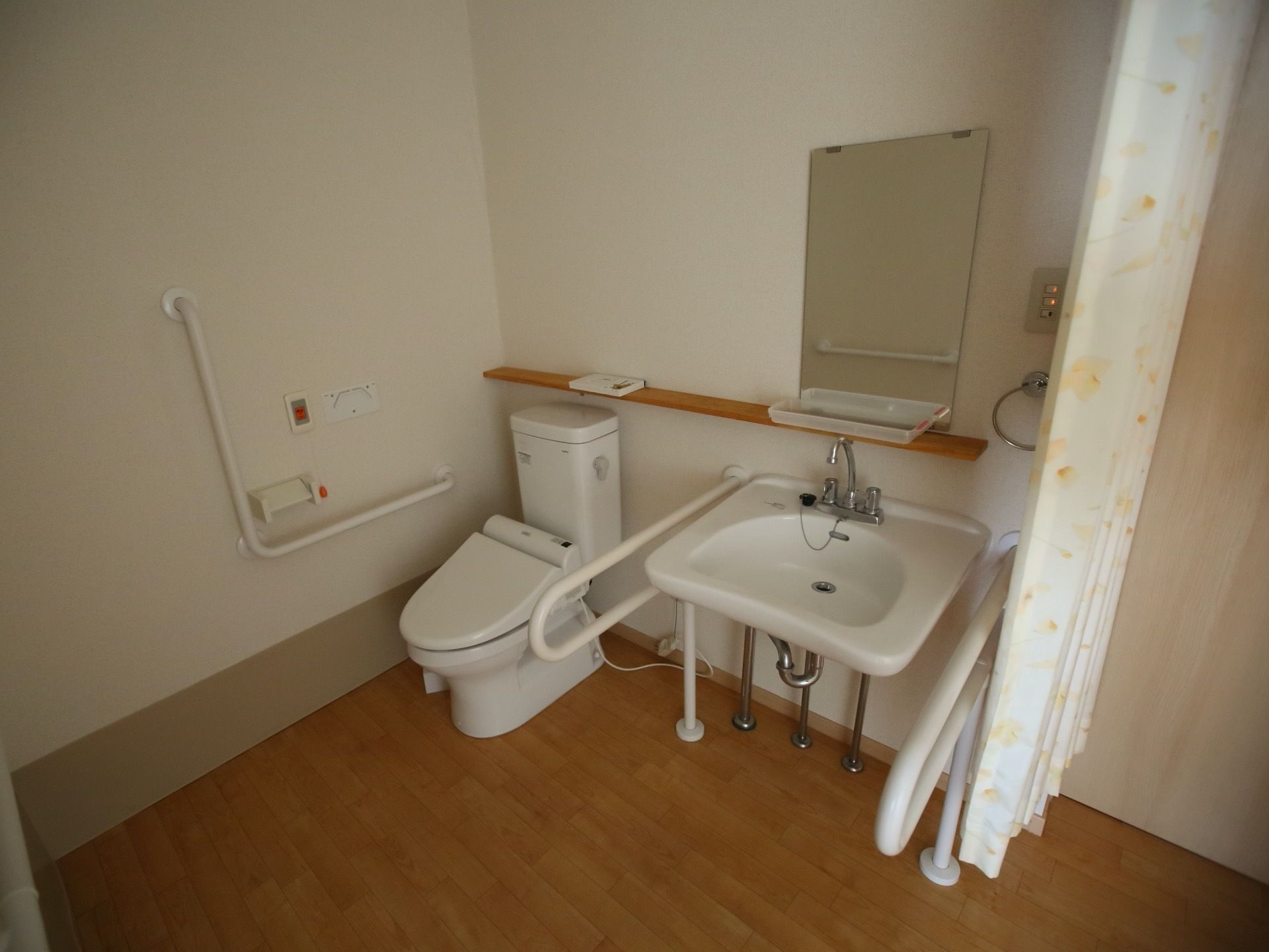 トイレとの仕切りにカーテンが使われている。カーテンを開けると右側の壁に沿って、手前から洗面台、洋式便座が並んでいる。