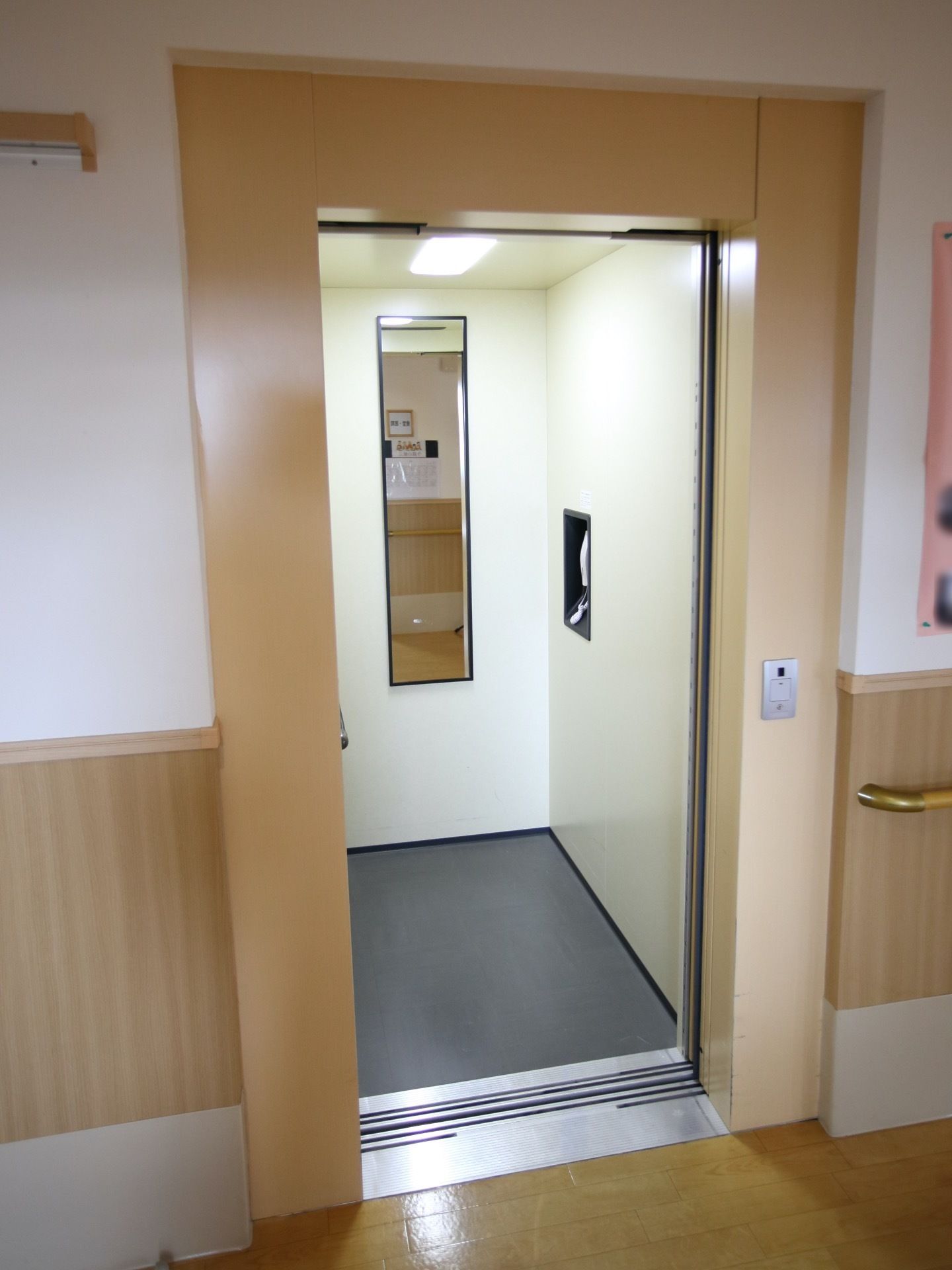 扉の外側を幅広のベージュ色の枠が囲んでいる。その枠に呼び出しボタンがある。間口は車椅子が通れる程度である。
