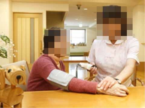 席について、スタッフに血圧を測ってもらっている入居者の女性