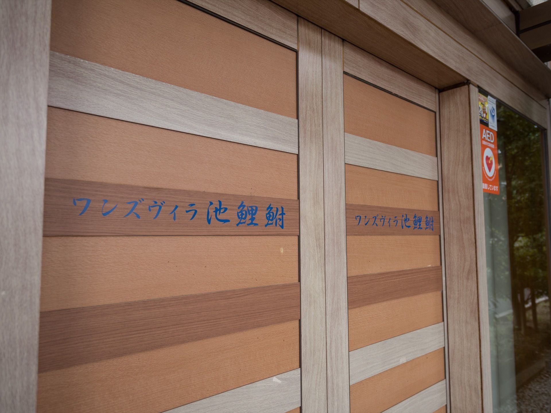 エントランスドアを外側から見ると、施設名が記載されている。青色の文字で描かれていて、落ち着いた雰囲気。