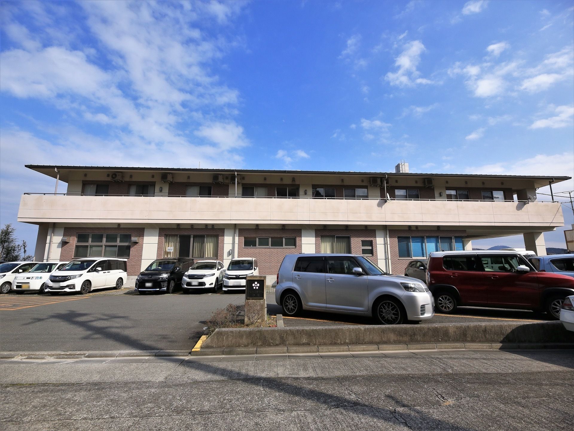 施設はブラウン色の外壁で、上の階にはベランダが設置されている。多くの車を駐車することができる駐車場を完備している。