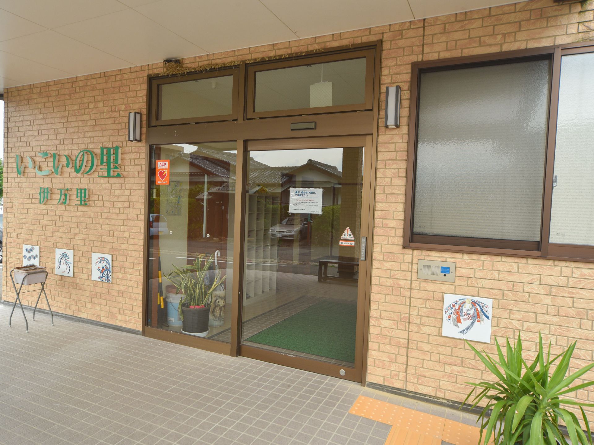 ベージュ色のレンガ調の外壁にガラス張りの自動ドアのエントランス。横には、大きな緑色の字で施設名を表示してある。