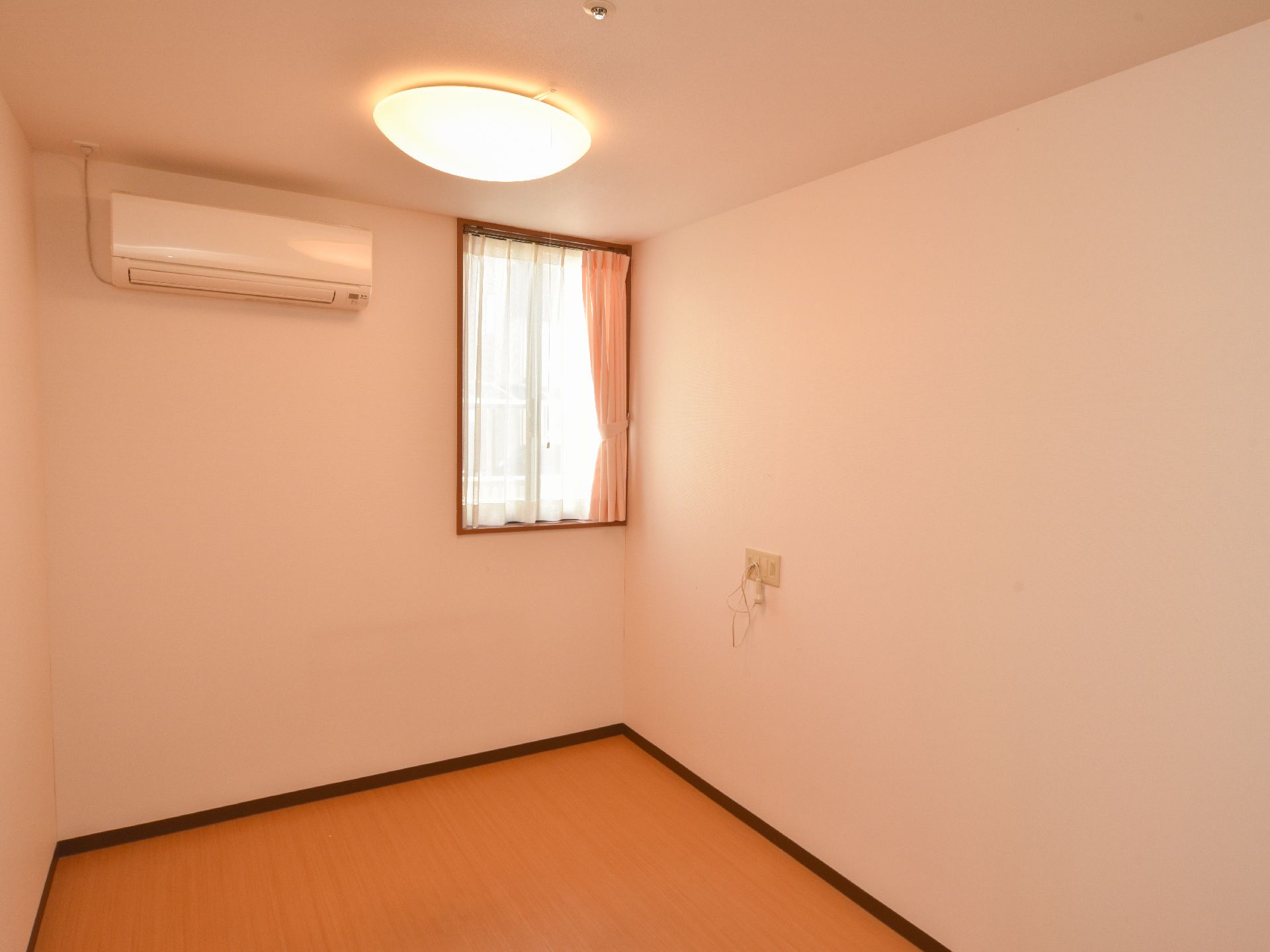 温かい色彩の内装の個室。正面の端側の上部に窓がある。エアコンが設置され横の壁にはナースコールが取り付けてある。