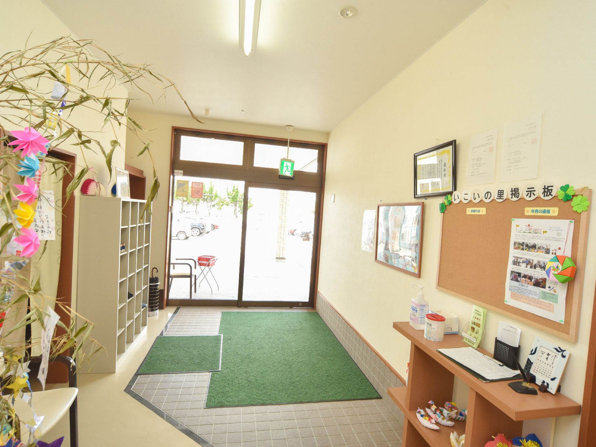 自動ドアの玄関出入口から入って、地面にはマットが敷かれている。右側には靴箱が設置され、上り口には棚が置かれ消毒液や書き物などが置かれている。