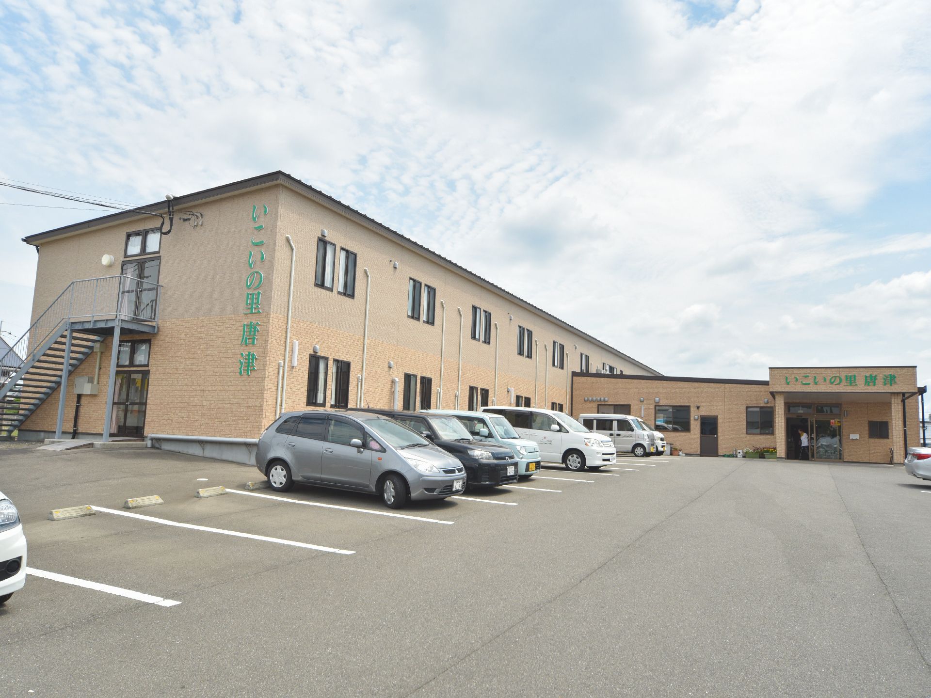 茶系の外壁の2階建ての施設。建物の前方は駐車場になっている。エントランスと建物の側面に緑色の大きな文字で施設名が表示されている。