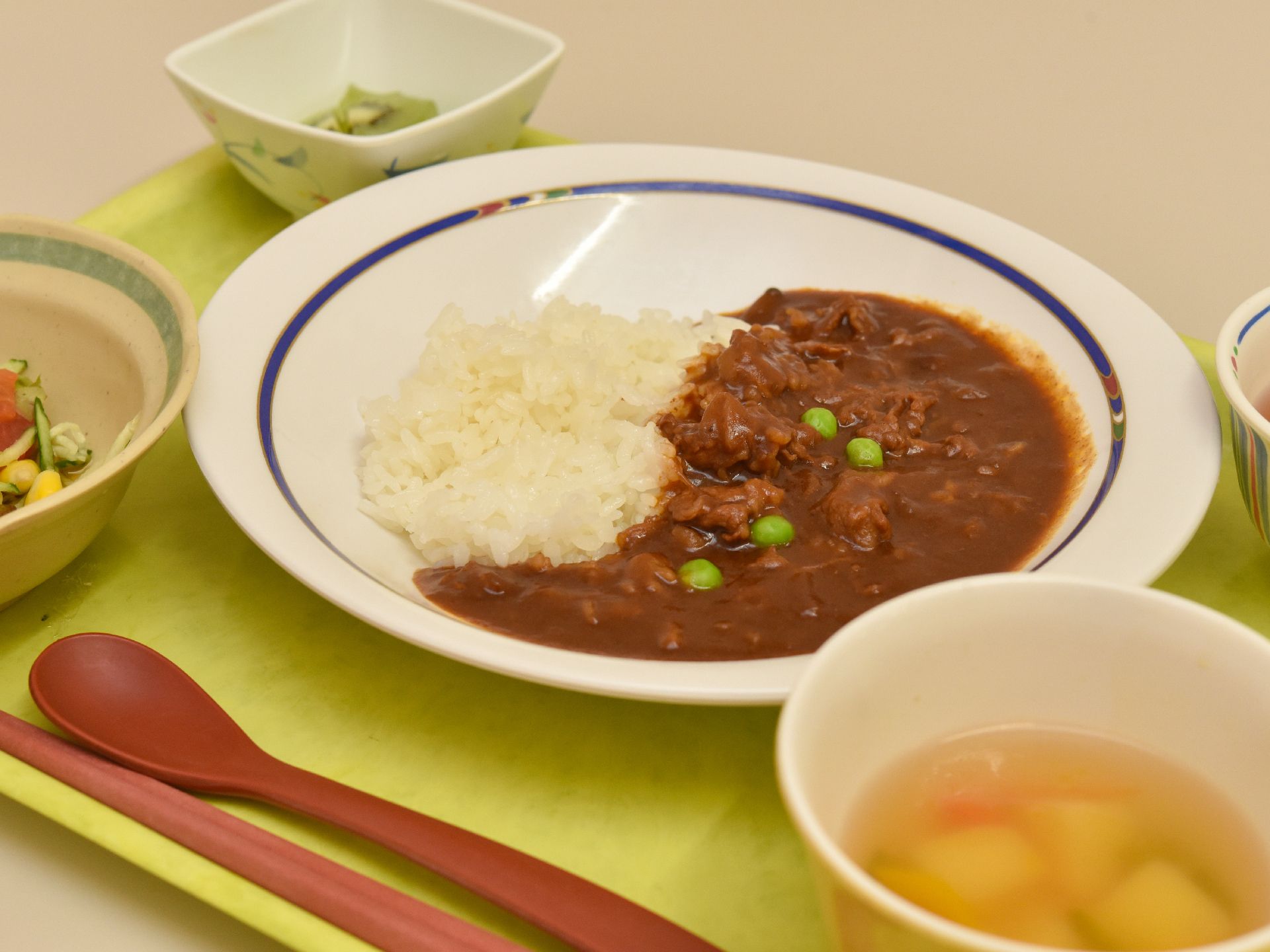 カレーライスに汁物と小鉢が２つにお茶、栄養バランスと品数を考慮された献立である。四季折々の食材で季節を感じながらの食事も出来る。