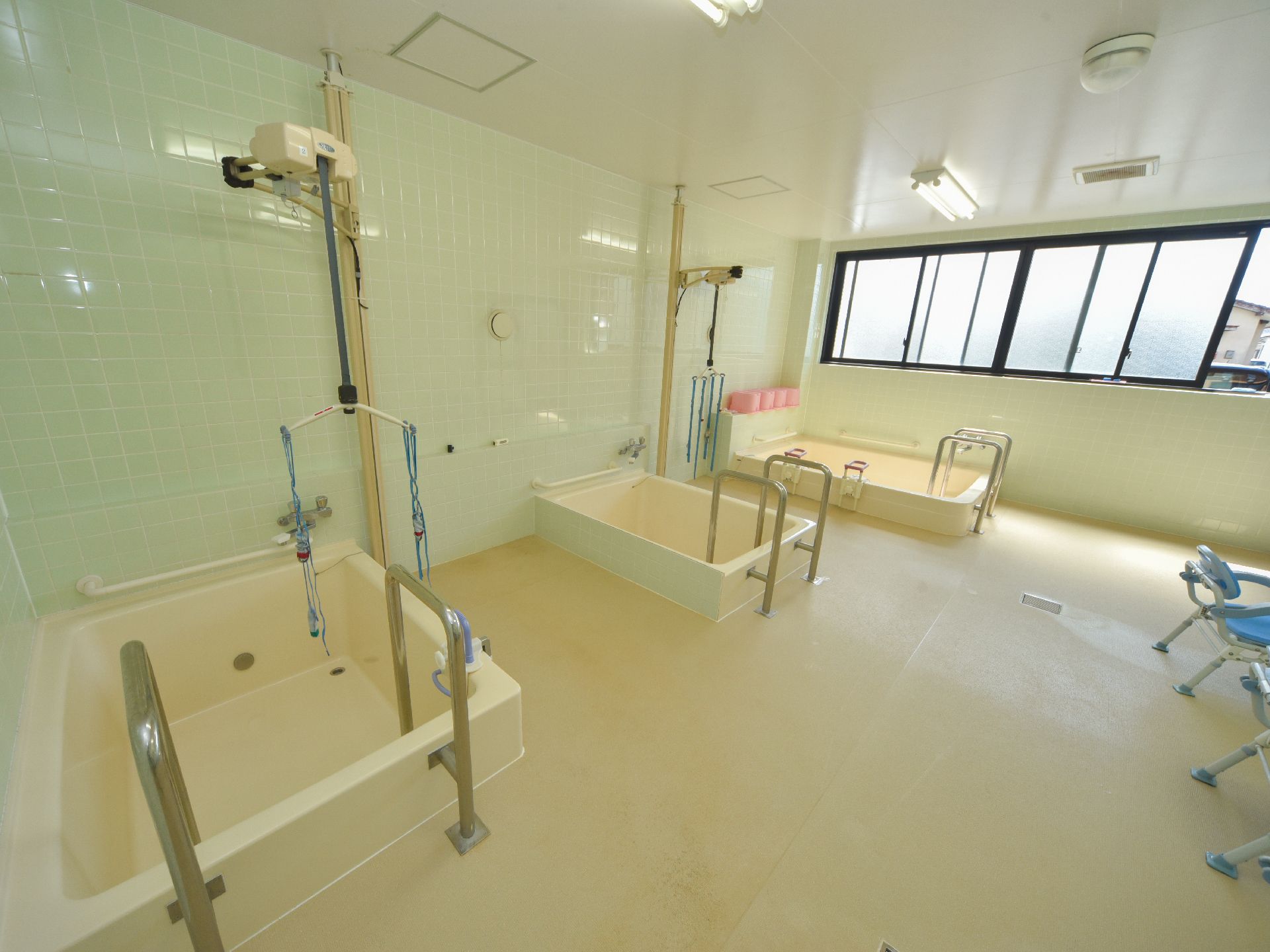 薄緑と茶系仕様の広々とした浴室。浴槽が3ヶ所あり、機械浴仕様になっている。正面は一面窓になっている。