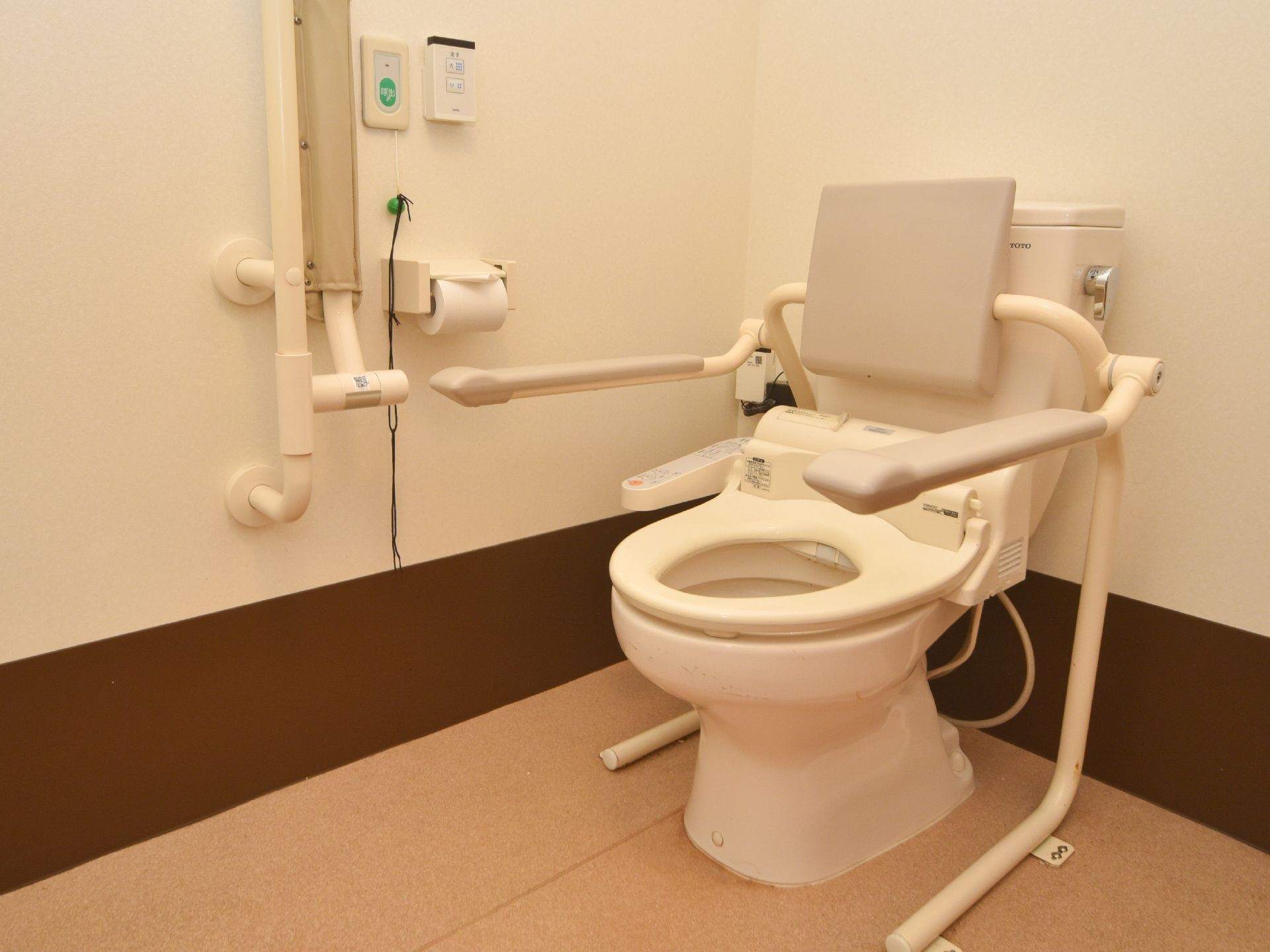 トイレの両サイドには、手すりがもうけてあるほか、貯水タンクのところに背もたれがついている。壁には、緊急時用のブザーが取り付けてある。