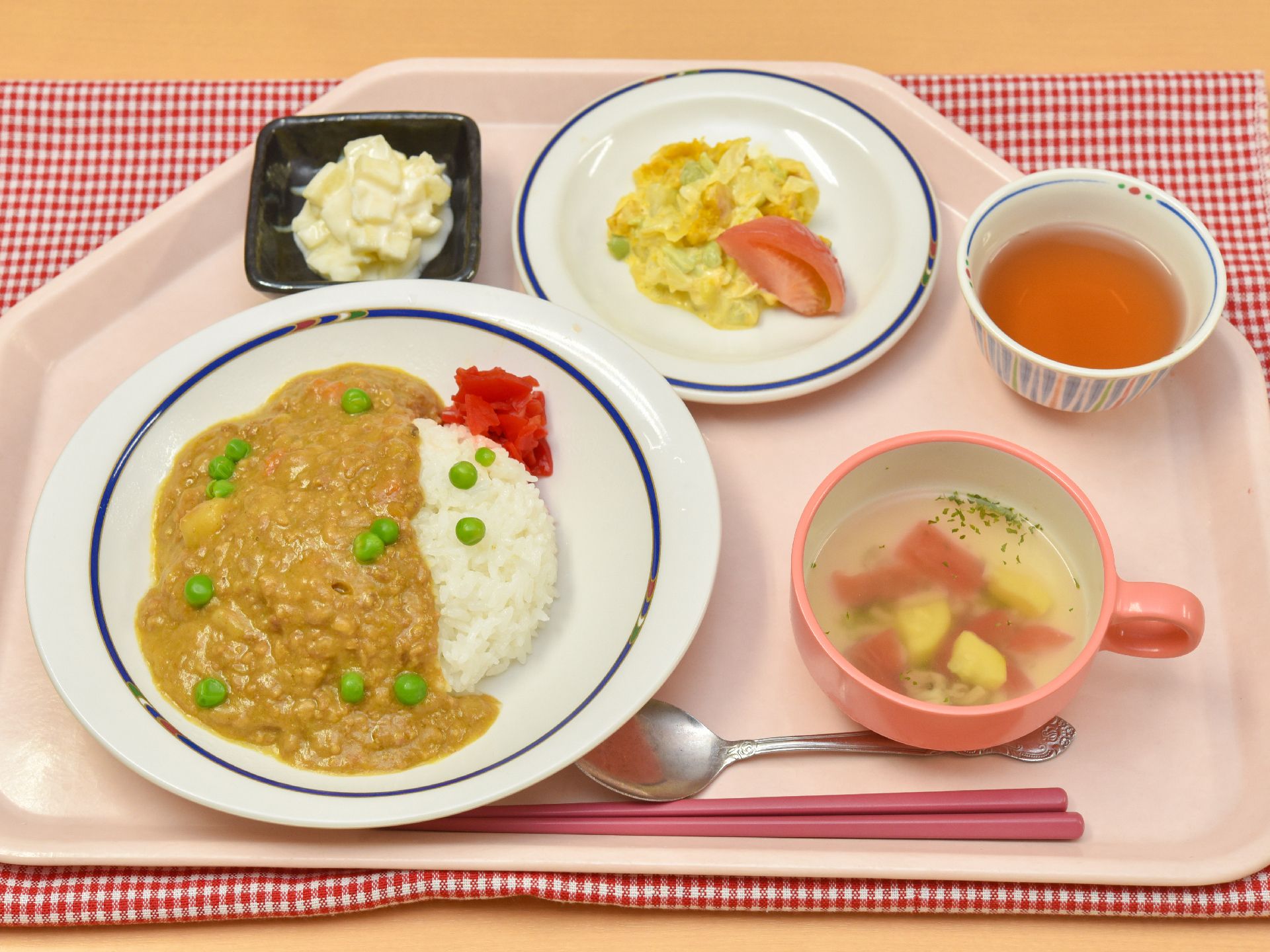 カレーライスにはグリーンピースの緑、漬物の色の赤が加わり、彩りよく盛り付けられている。スープ、卵炒め、お茶などが一緒に盆に乗っている。