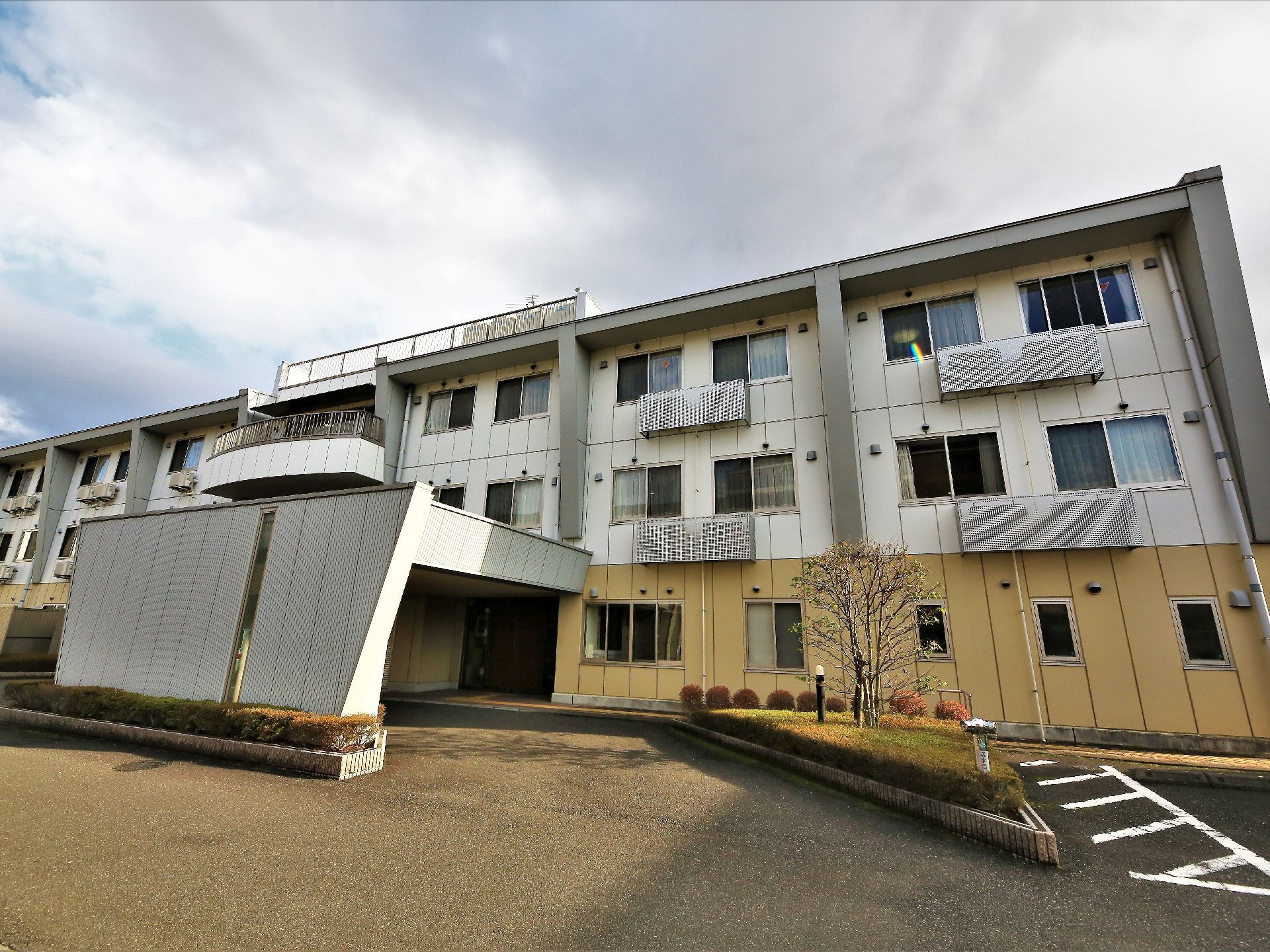 三階建ての大きな建物がある。一階部分の壁は黄色に塗られ、他は白い壁になっている。玄関部分は壁とルーフで覆われている。