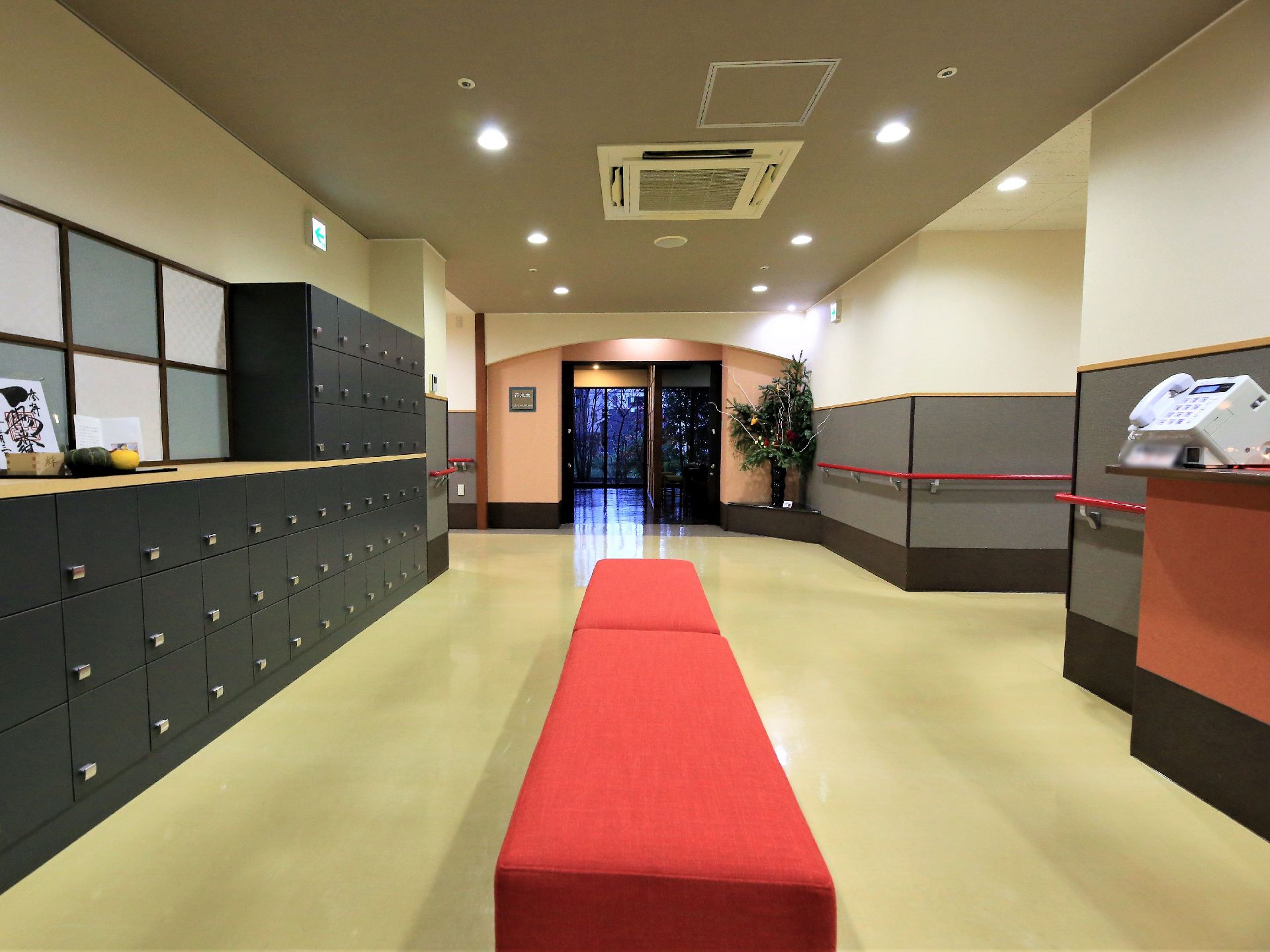真ん中に赤いベンチが置かれた広い玄関ホール。壁際には扉のついた、黒い大きな下駄箱が並んでいる。突き当りは窓になっている。