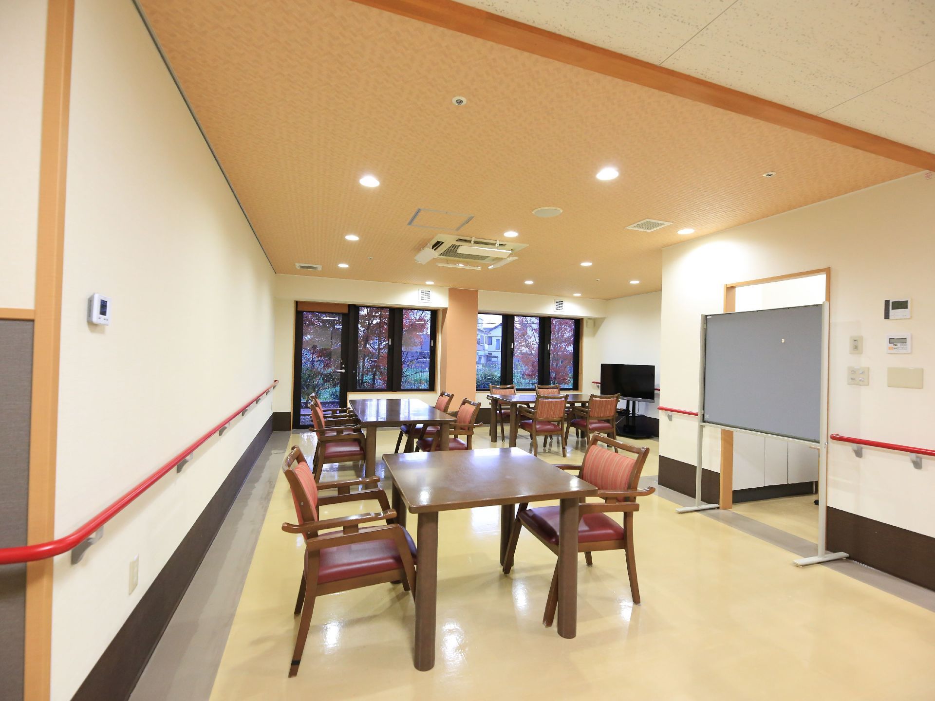 ひじ掛けのついた椅子とテーブルが並んでいる広い食堂。壁は一面窓になっている。ホワイトボードとテレビが置かれている。