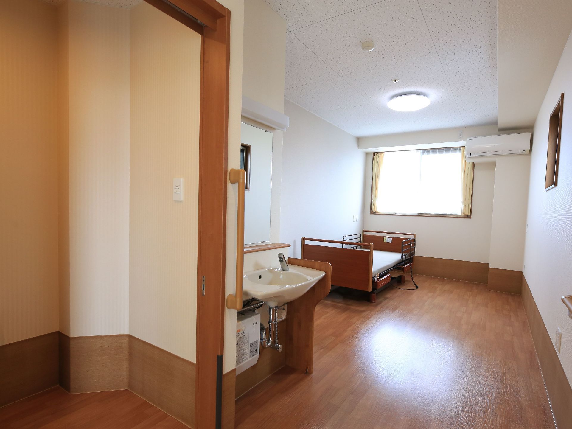 部屋の奥側にベッドが１台置かれており、壁にはエアコンが取りつけられている。また、入口側には、洗面台が設置されている。