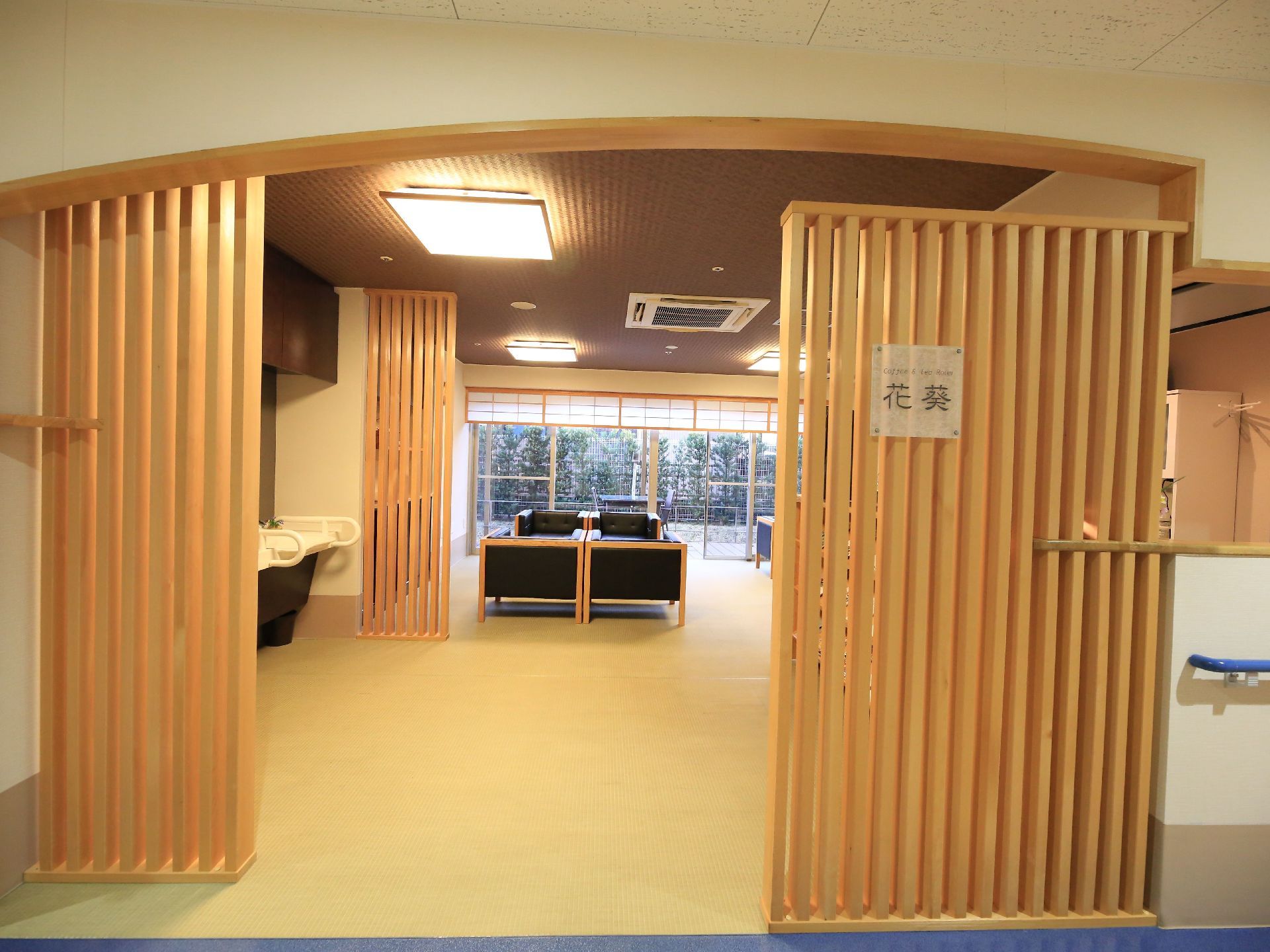 木でできた仕切りの先に広い空間があり、複数のゆったりしたソファが設置されている。空間奥には大型の窓があり、広い庭の風景が臨める。