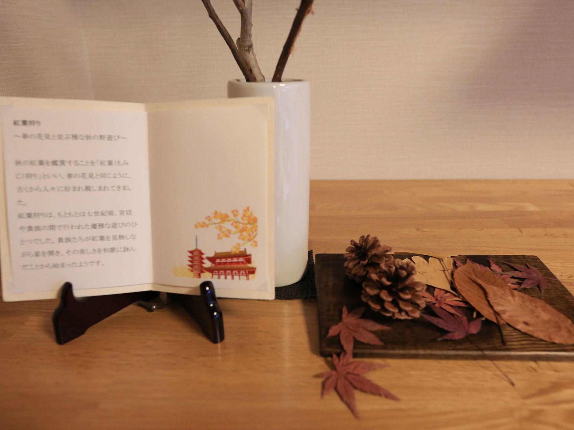 松ぼっくりや紅葉、銀杏などの葉が、台座の上に丁寧に折り重なった形で配置されている。隣には、「紅葉狩り」に関する説明書きが添えられている。