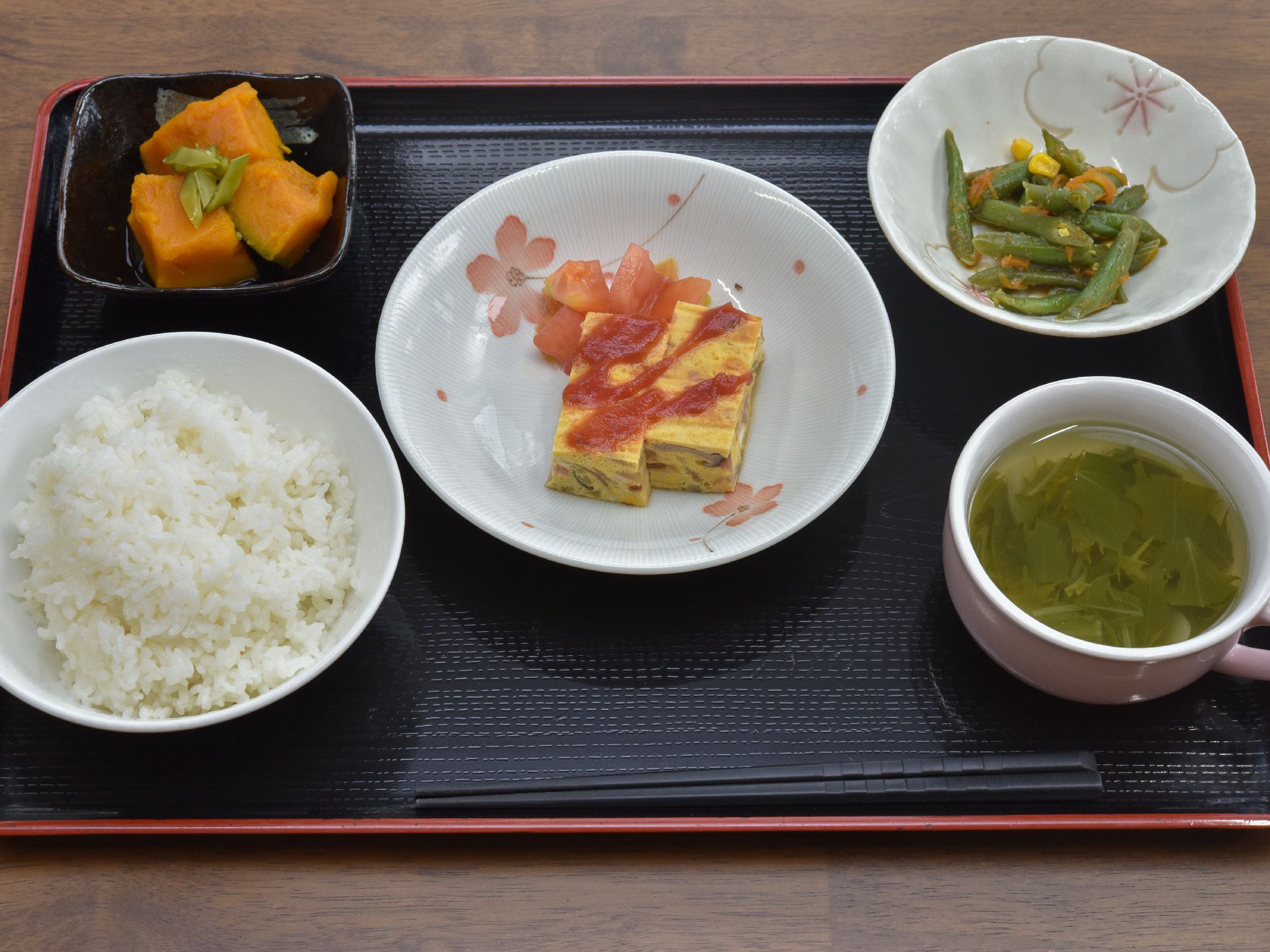 盆の上にごはん、かぼちゃの煮つけ、たまごやき、インゲンのあえもの、スープなどがのっている。食べやすい一口サイズになっている。
