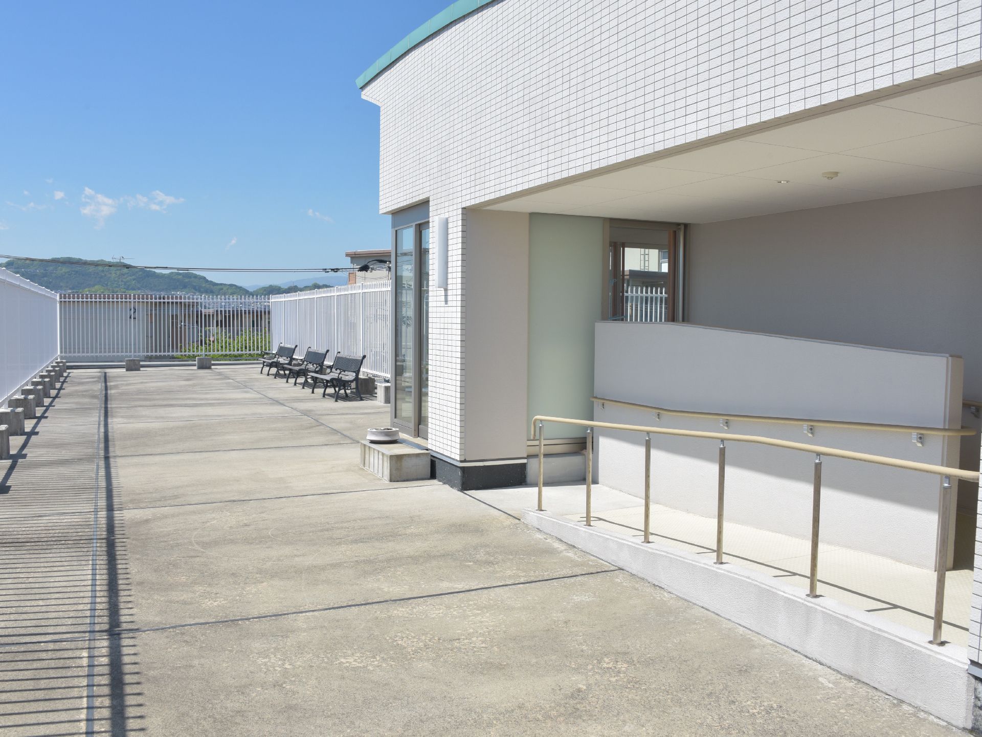屋上へと出ていくところにはスロープがあり、転倒防止用の手すりがある。屋上の端の方にはベンチがいくつか並んでいる。