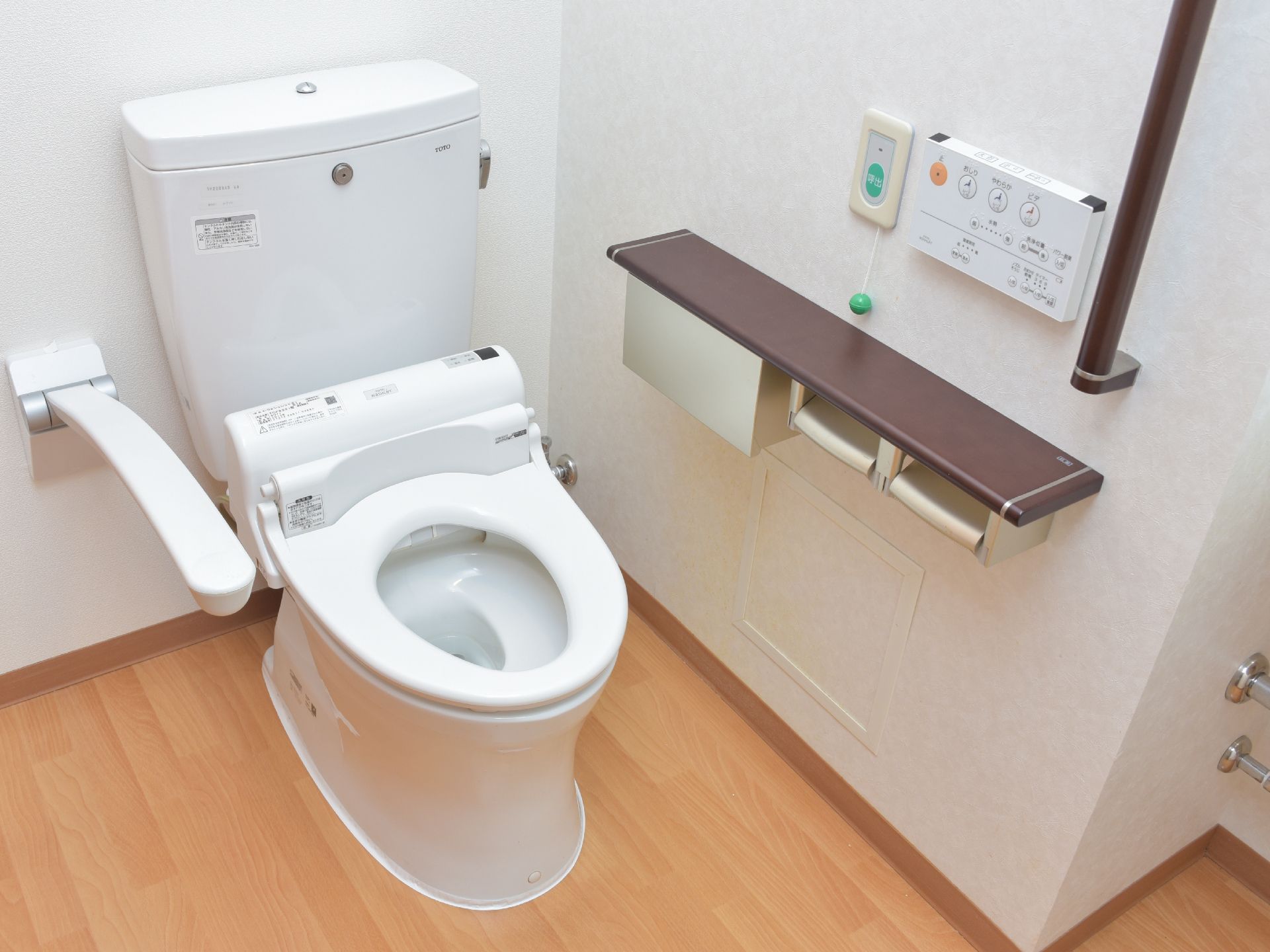 固定式と跳ね上げ式の手すりがついた、トイレ。ウォシュレットの操作パネルも壁についており、操作がしやすい。