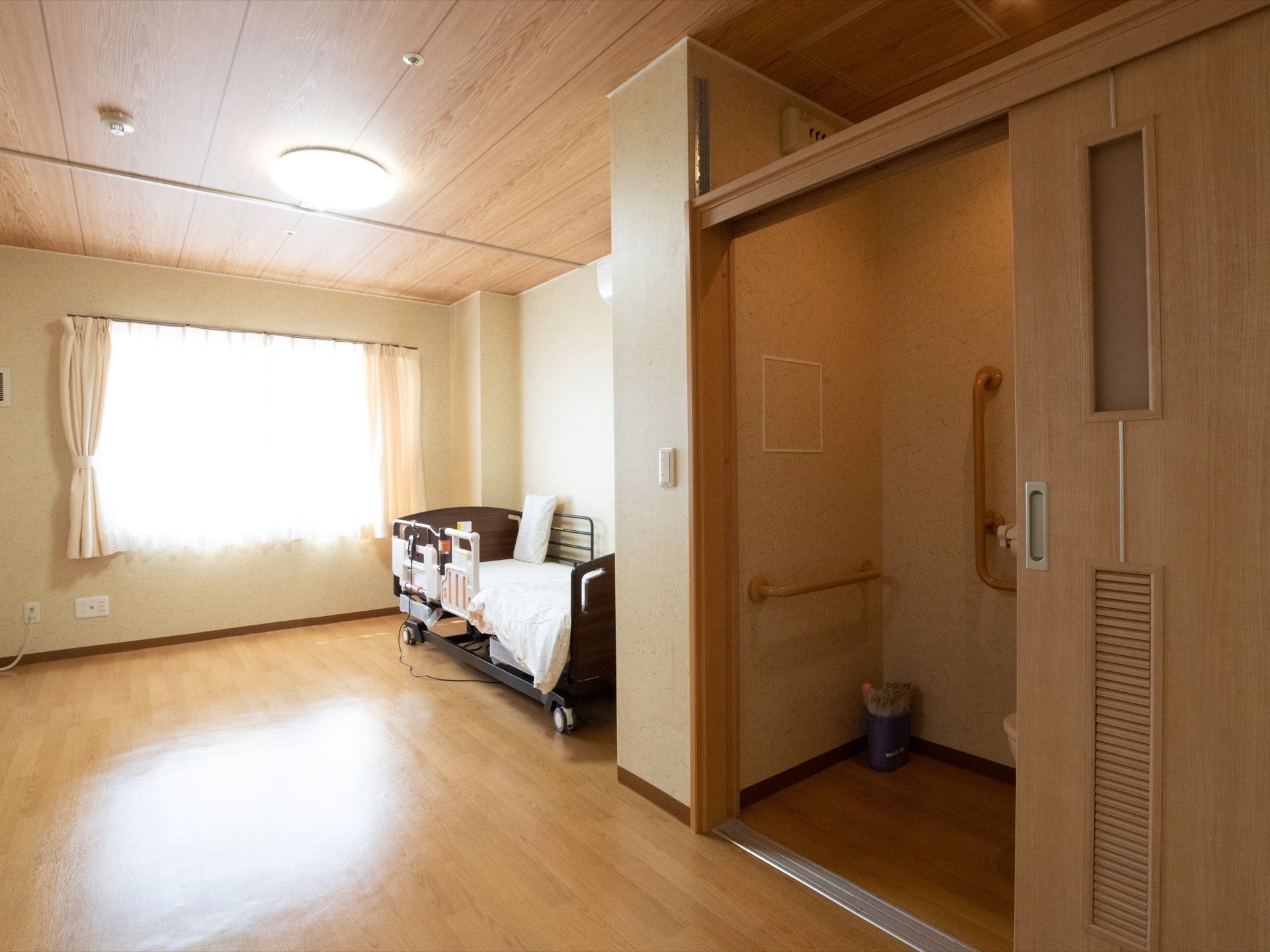 居室内にトイレが設置されている。出入り口は大きく開く木目調の引き戸となっていて、床面はフラットである。