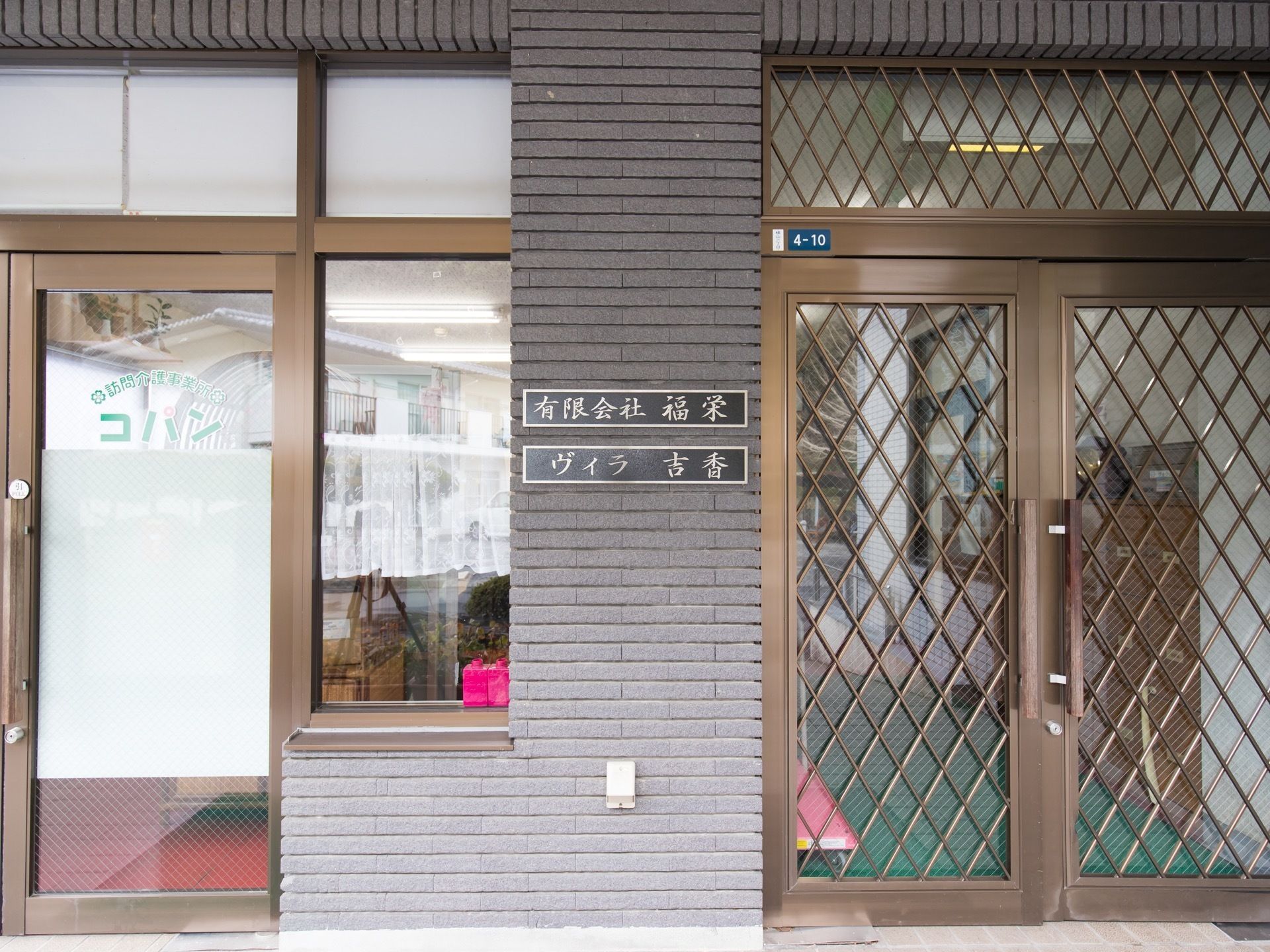 施設の入口の隣に、訪問介護の事務所がある。壁には黒字に金で施設名が書かれたプレートが掛けられている。