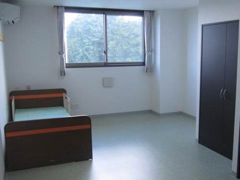 奥の壁に窓があり、黒色のベッドとタンスが設置された居室