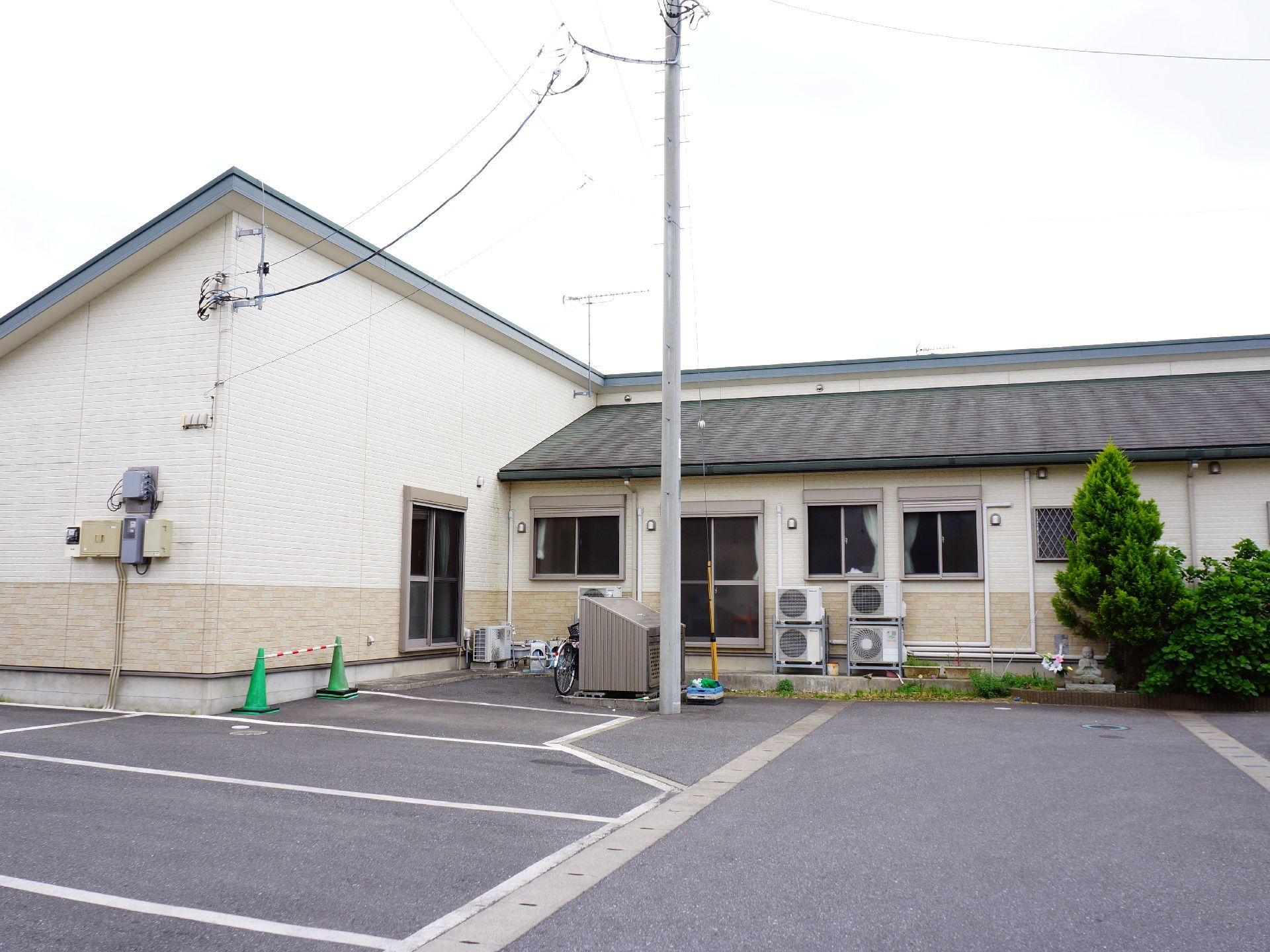 施設の外観はオフホワイトの落ち着いた雰囲気である。外には車の止めることのできる駐車スペースが設けられている。