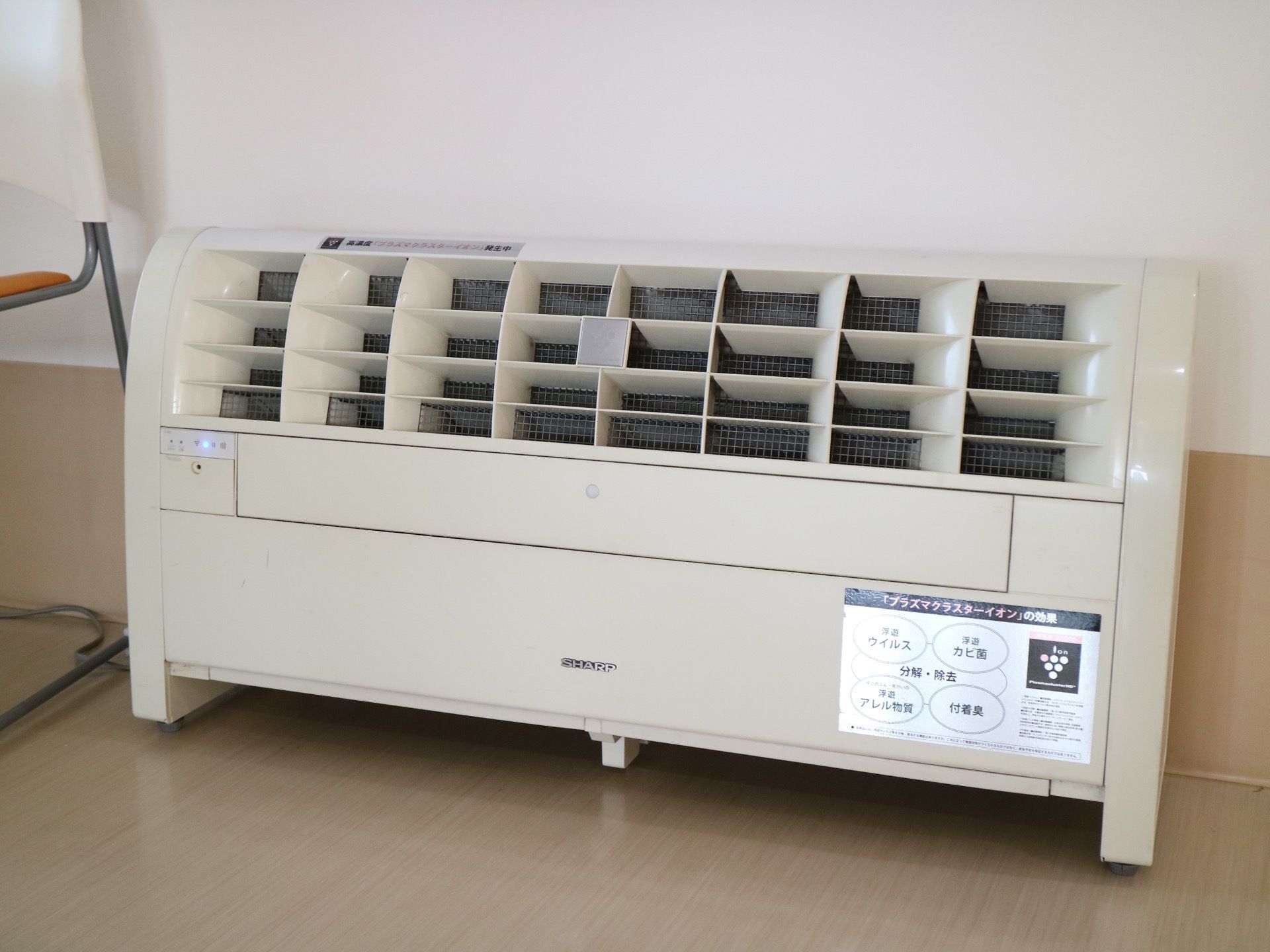 某有名メーカーの特色ある空気清浄機が、フローリングに設置されている。壁際で、椅子が横に置かれている。