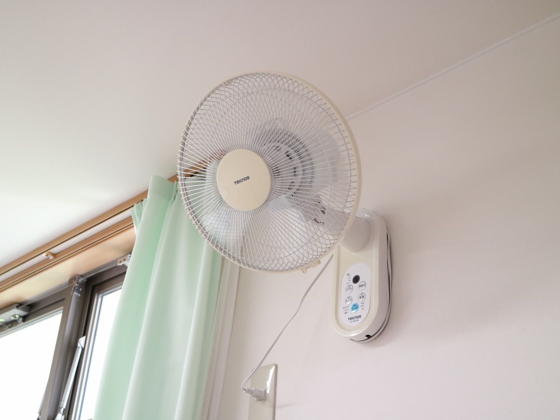 白い壁に設置された窓のそばに扇風機が取り付けられている。空気の対流を促し、心地よい風が流れるようになる。