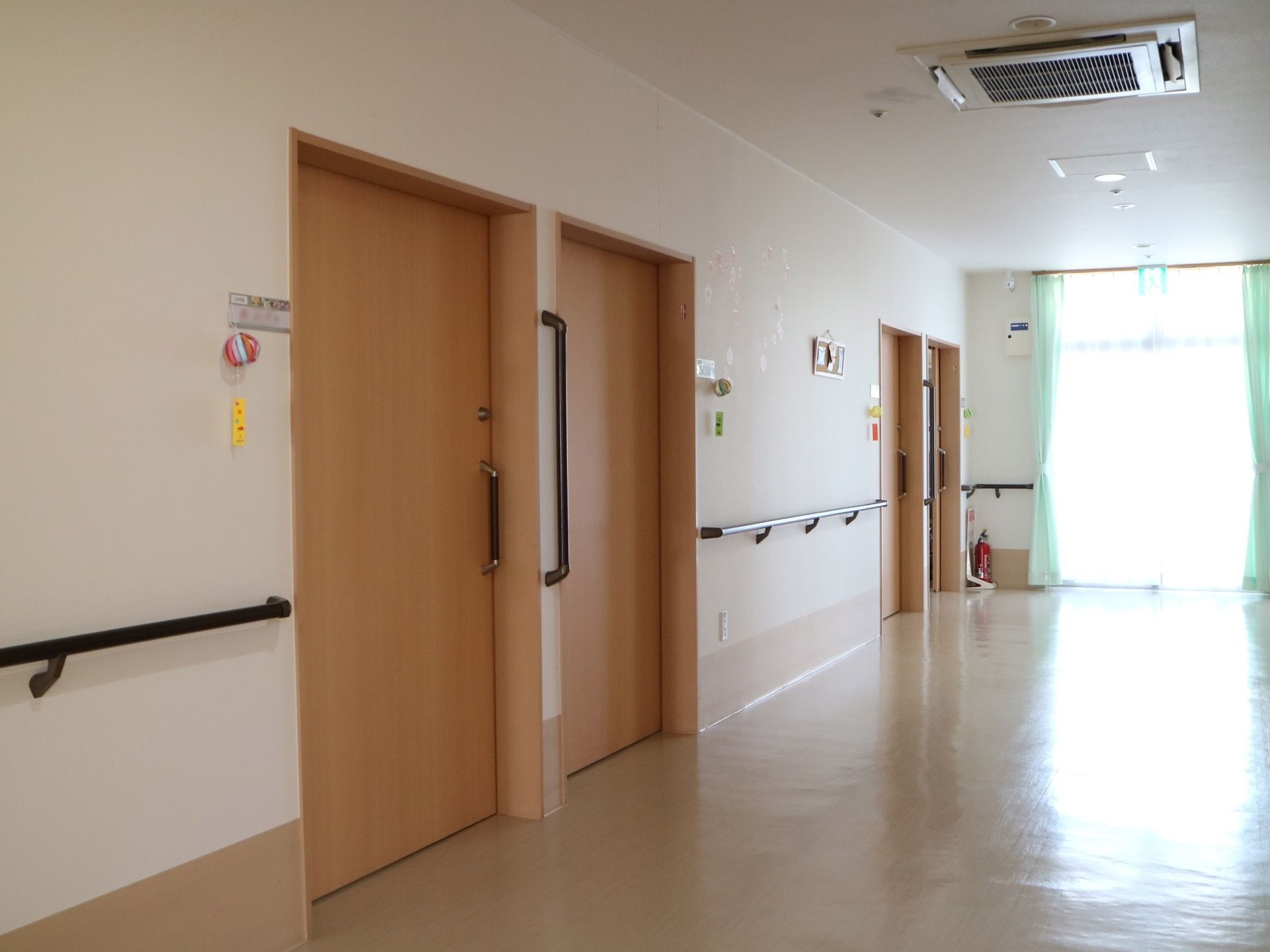 居室前の廊下には、消火器が置かれている。居室扉は隣り合い、中間の壁には縦型の手すりがある。