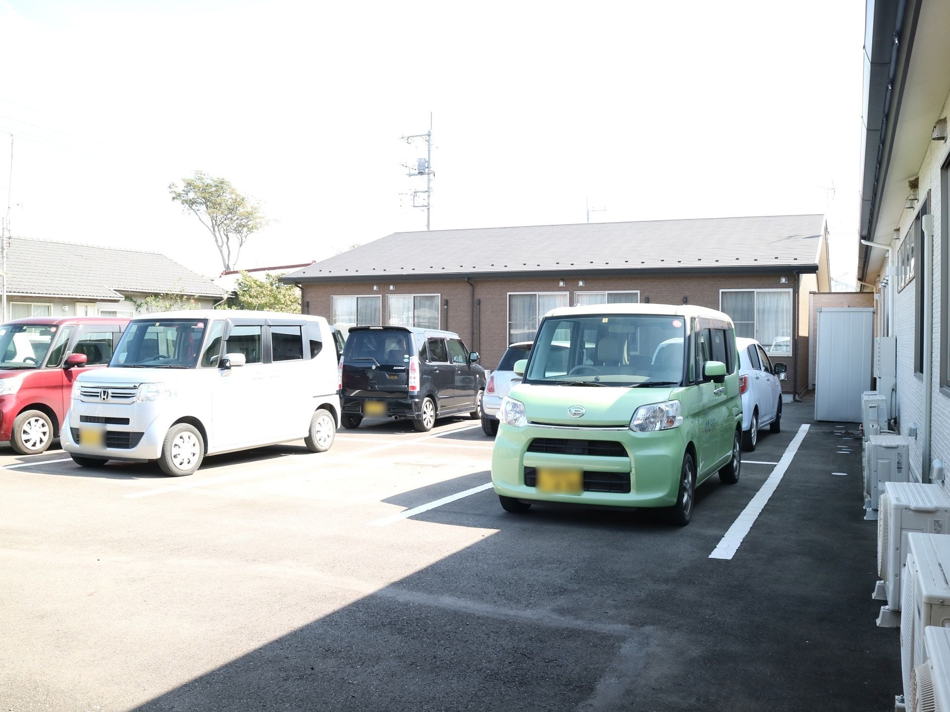 各居室に設置されているエアコンの室外機のそばには、駐車場が完備されている。数台の乗用車が停車している。