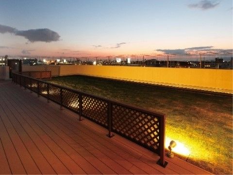 ライトに照らされている、柵で囲まれた屋上の芝生スペース