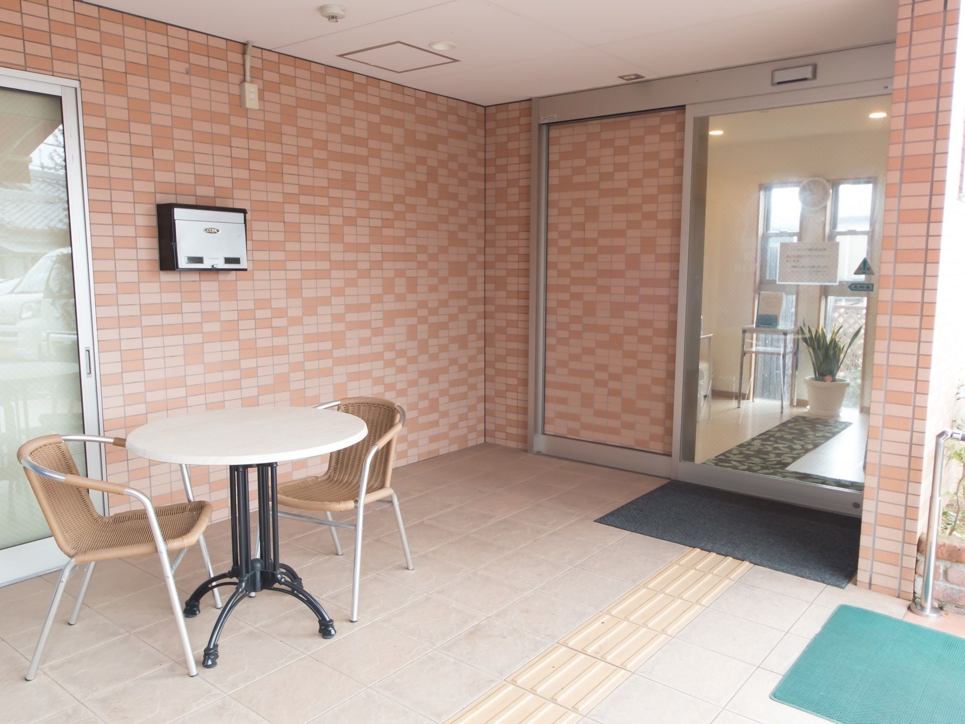 玄関の外には屋外用の座席がエクステリアを兼ねて置かれている。壁は赤茶色をしたレンガ風のデザインになっている。