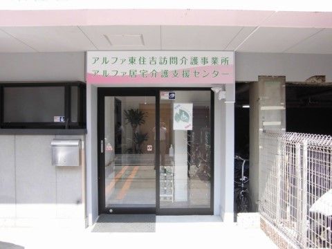 右側に白い柵があり、上部に施設名が書かれた看板が設置されている玄関