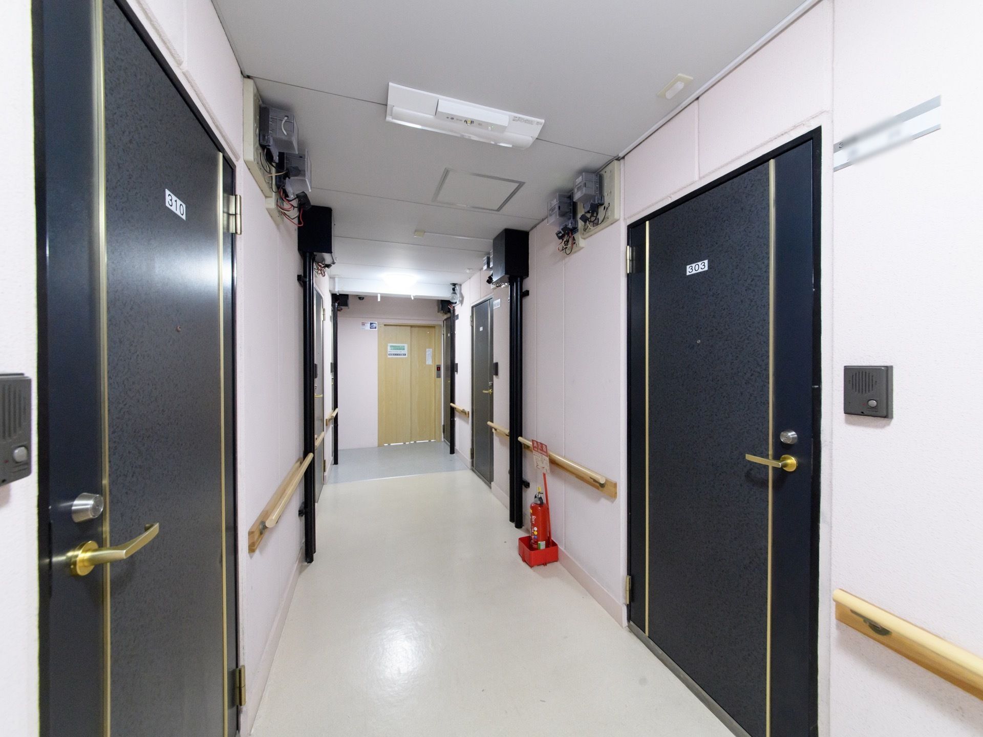 ダークブルーの居室の扉が、通路の両側に並んでいる。白い小さなプレートには、部屋番号が書かれている。壁際に消火器がある。