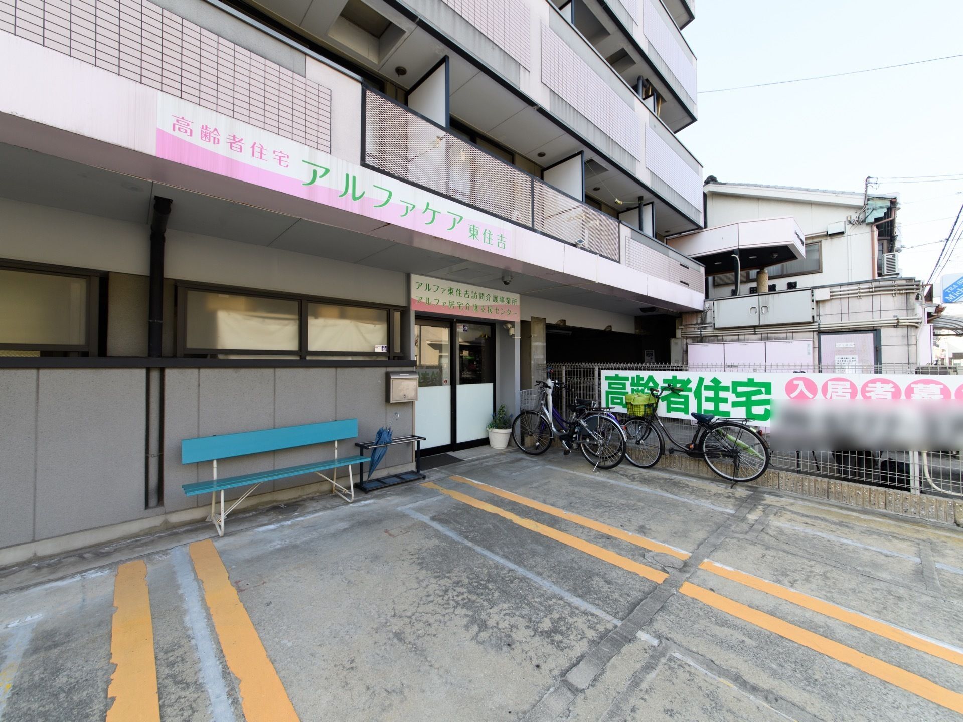 駐車場には、黄色のラインが２本引いてある。その横にはフェンスがあり、緑色の大きな文字が書かれた看板が取り付けられている。