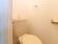 コンパクトなスペースに設置されたトイレは、白とベージュでまとめられた明るいデザインである。円形のタオル掛けが右側にある。
