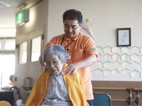 男性スタッフに肩をマッサージされている、椅子に座った入居者様の女性