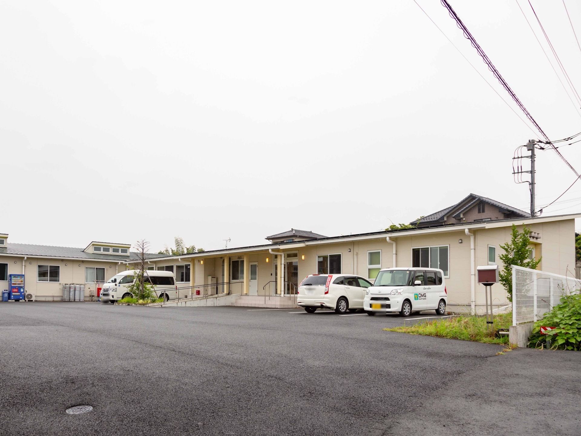 オフホワイトの１階建ての建物は、シンプルで清潔感に溢れている。敷地内は、広々としたスペースを設け、駐車場を備えている。