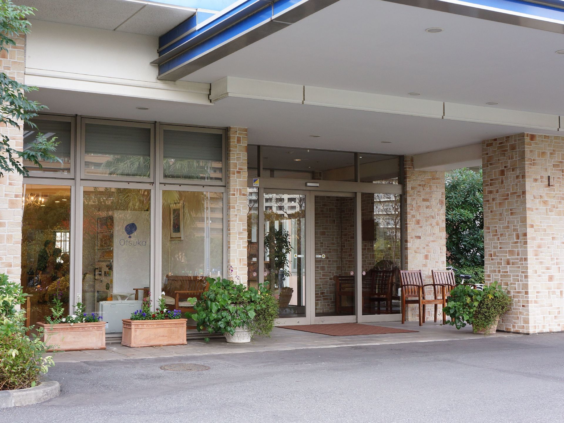 レンガ調の柱がスタイリッシュな雰囲気の玄関はガラス張りになっており、入り口には椅子や鉢植えが置かれている。