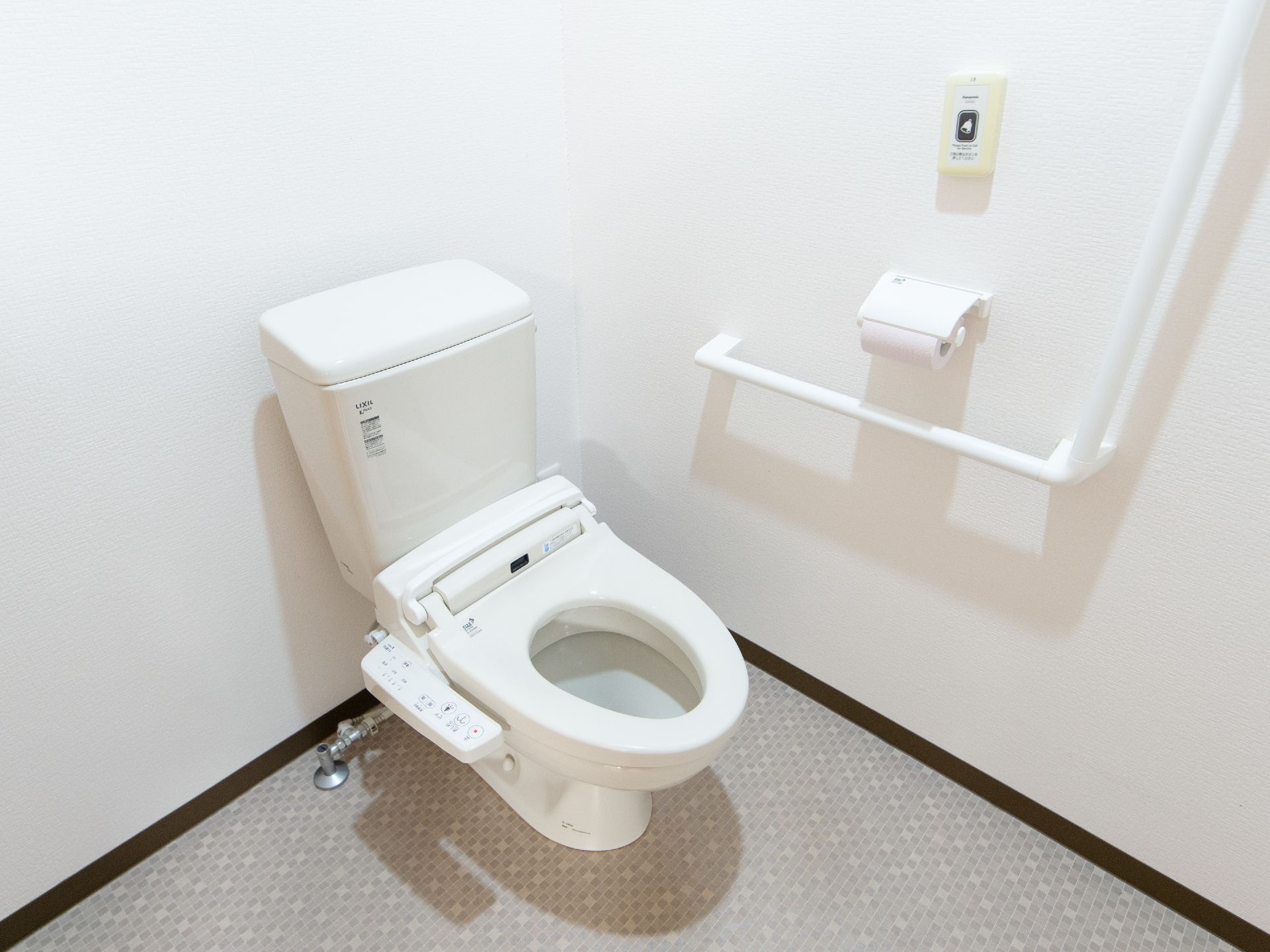 白を基調とした清潔感のあるトイレである。壁にはＬ字型のしっかりとした手すりや緊急連絡ボタンが備わっている。