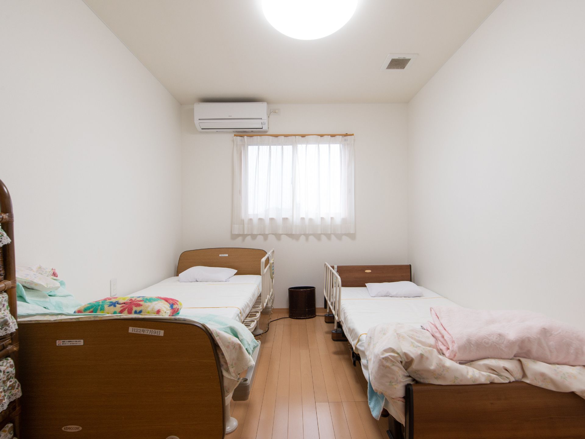 介護用ベッドが二つ並べられている居室である。居室には窓があり、エアコンが備わっている。整理かご棚が置かれている。
