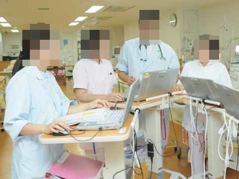 高テーブルの上にそれぞれパソコンを設置し、ミーティングをしている四人の医療スタッフ